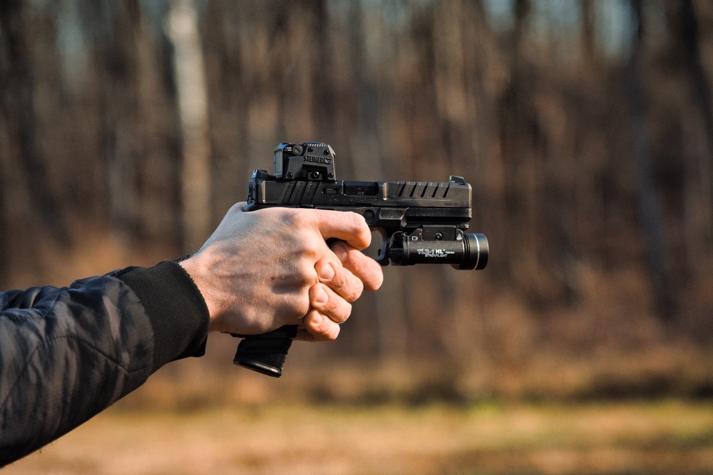 Shown is a photo of the author testing the Steiner MPS reflex sight mounted atop a pistol — in this case a Springfield Echelon. The MPS uses a mounting footprint similar to the Aimpoint ACRO footprint. That means the optice does need an adapter plate. However, it does not interfere with the rear sight.
