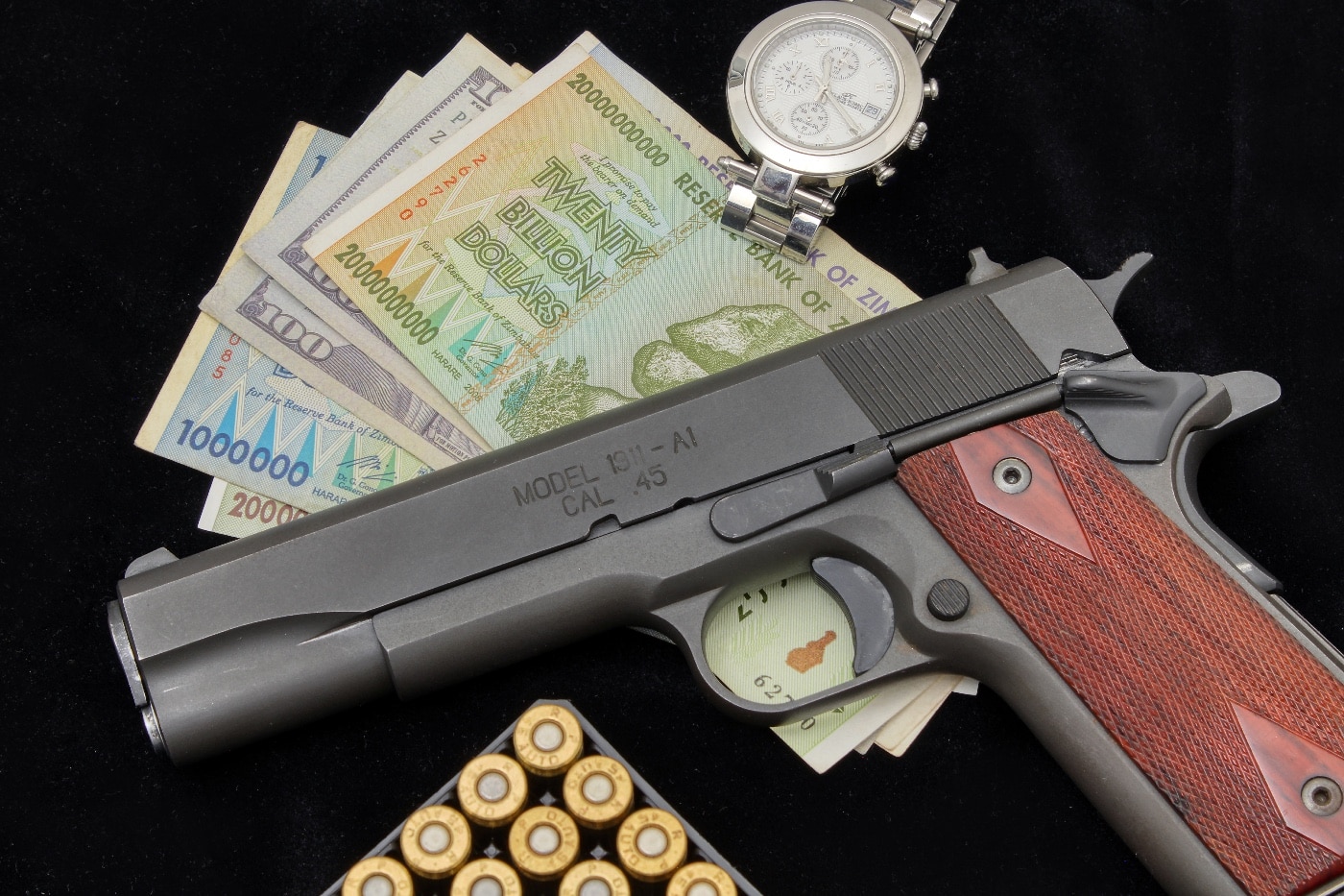 In this photo we see a M1911A1 pistol chambered for the .45 ACP cartridge. The handgun was the standard sidearm of the United States military. Also shown in the photo is ammunition, a wrist watch, paper currency money and more. M1911A1 pistol as an investment