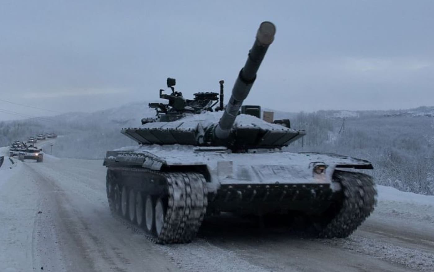 This image shows a Russian T-80BVM tank driving in a column down a road inside the Arctic Circle. The tank and road are covered in snow and ice due to the winter conditions.