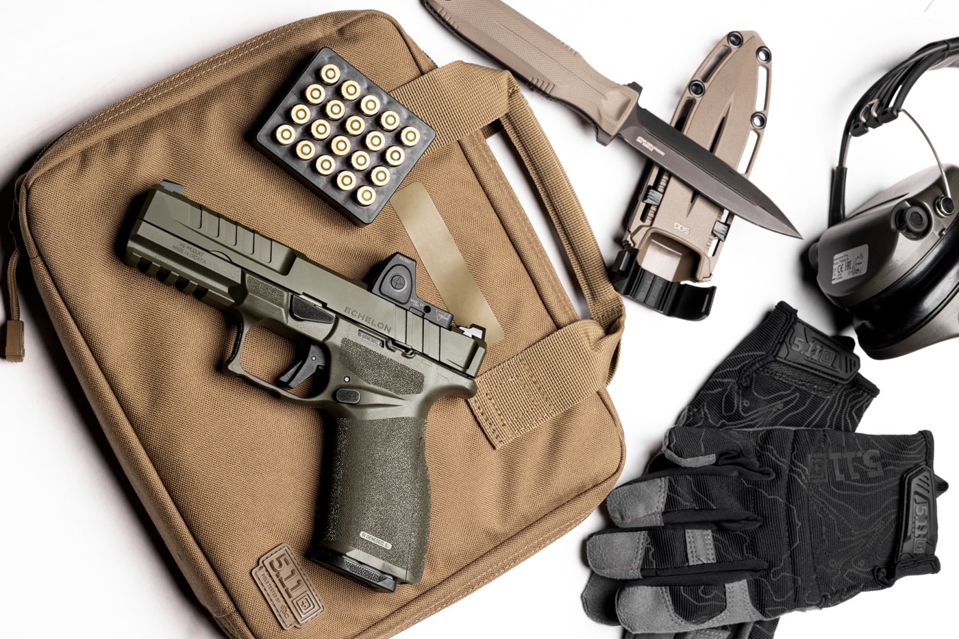 In this photograph, we see the new Springfield Armory Echelon in OD Green along with a variety of shooting accessories that one might take to the shooting range. These include a semi-automatic pistol case, shooting gloves and hearing protection.