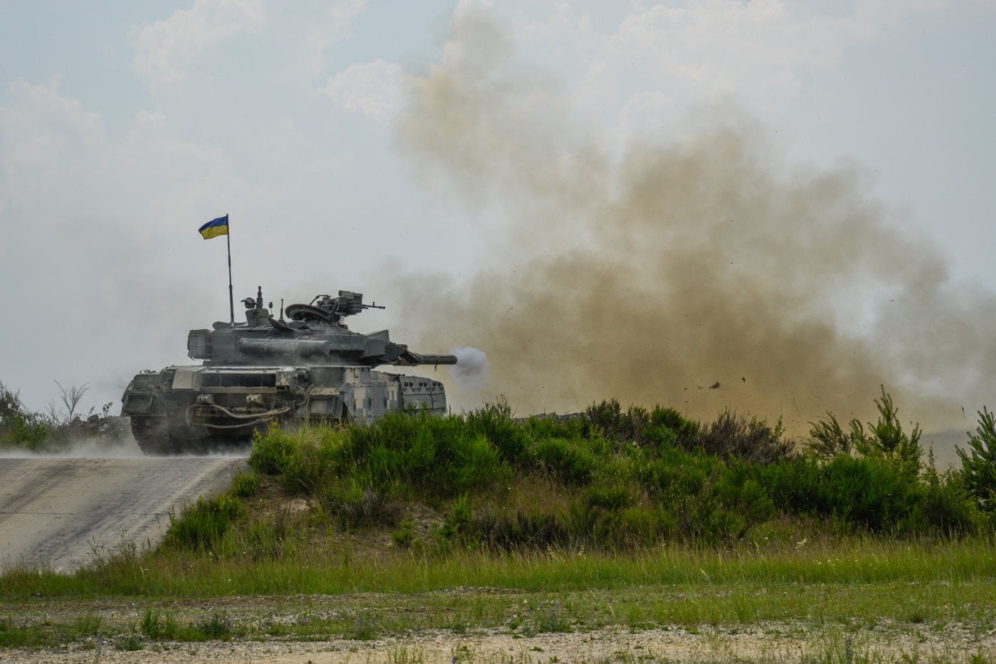 Here we see T-84 tank troops train with main gun on the firing range. Smoke fills the air as the recoil rocks the tank backward in its firing position.