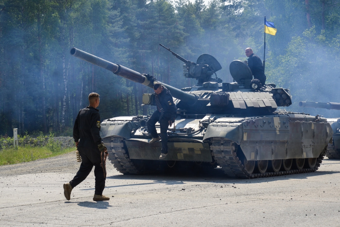 In this digital image, we see three Ukrainian soldiers dismount a T-84 tank after gunnery range training. Smoke from the tank engines hangs in the air.