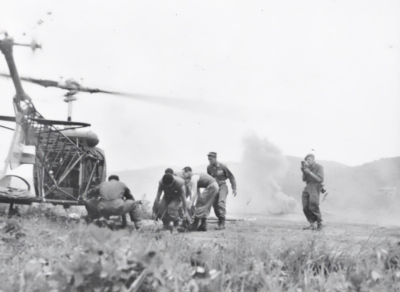 US Army Bell H-13 arrives at MASH unit as artillery explodes in background