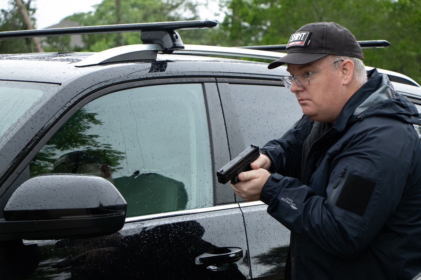 In this photograph, we see Richard Johnson, the Managing Editor of The Armory Life, with a Springfield Armory Hellcat 9mm pistol. The semi-automatic pistol is perfect for self-defense and personal protection. Richard Johnson is wearing a ballcap hat and a weatherproof jacket. It is raining.