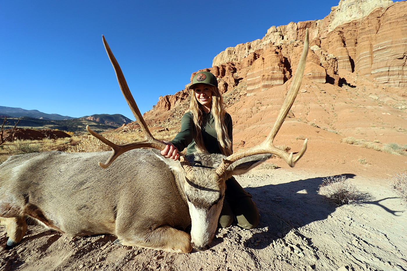 In this photo, the author is photographed kneeling next to the large mature buck mule deer she hunted with a Springfield Armory bolt action rifle chambered for the 6.5 PRC cartridge. She shows us how to hunt mule deer in this article.
