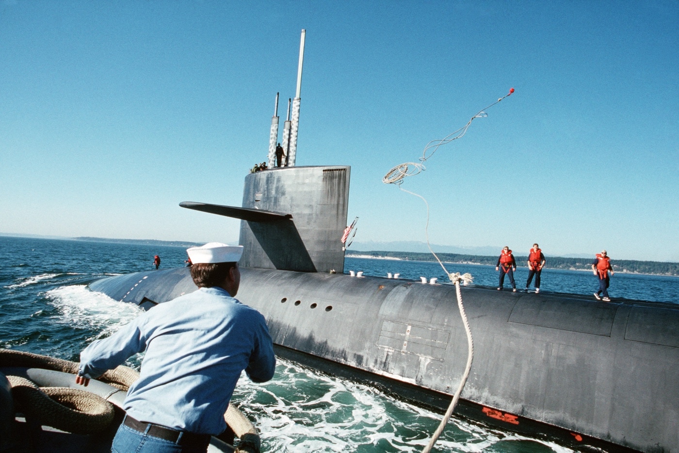 sailor on tug boat throws line to sailors on USS Alabama