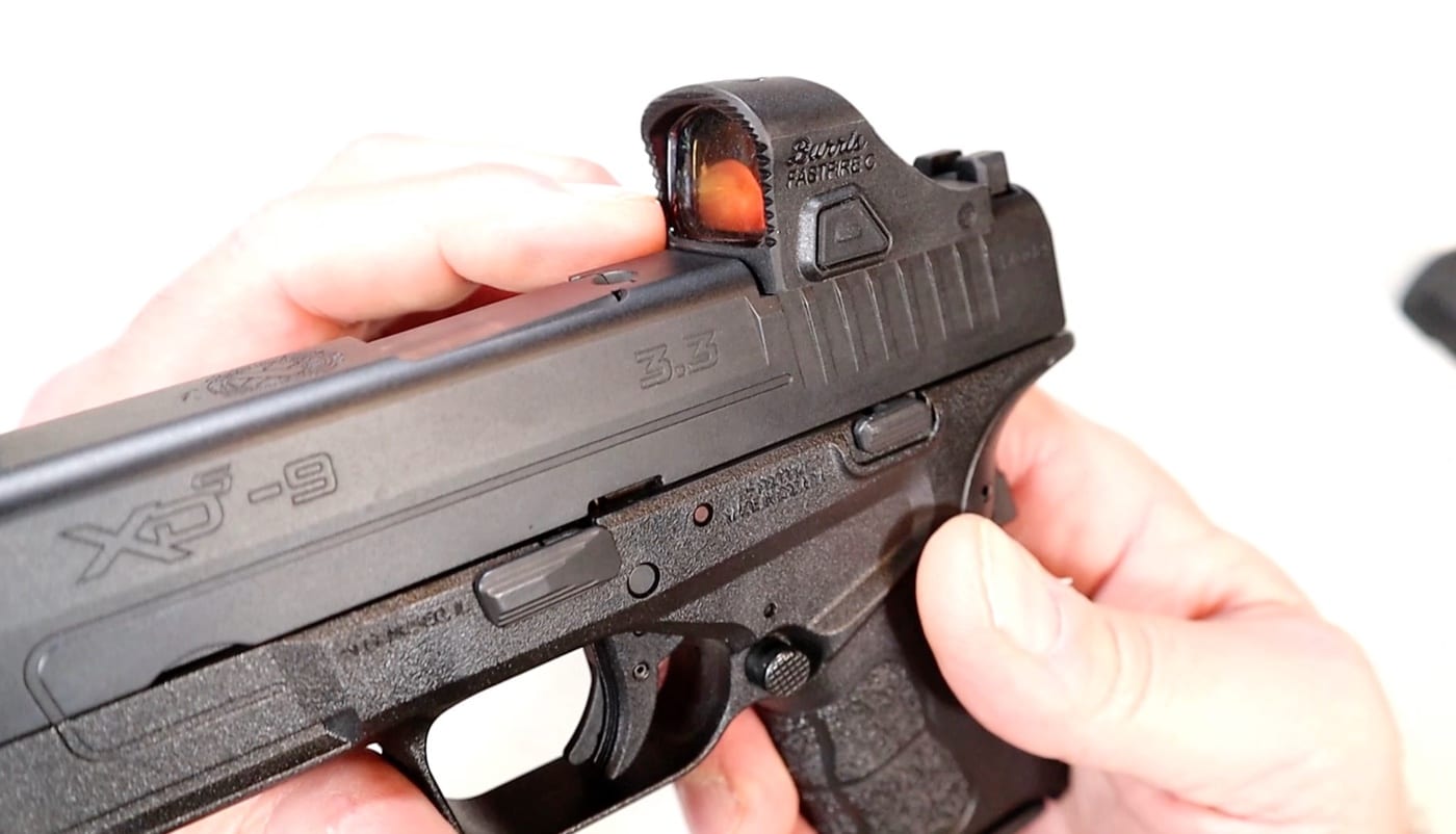 The author examines whats included with Burris FastFire C package. The box includes a battery, cleaning cloth and protective cover. It is designed specifically for sub-compact and micro-compact CCW pistols.