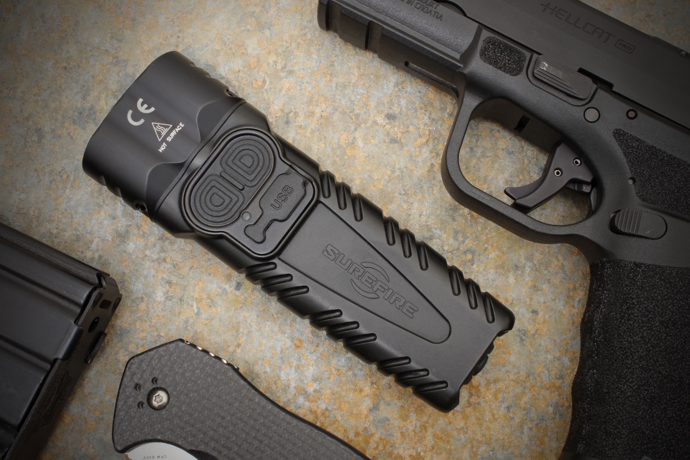 Shown here is the SureFire Stiletto Pro II review everyday carry flashlight with rechargeable battery along with other EDC gear including a Springfield Armory Hellcat Pro 9x19mm Parabellum semi-automatic pistol.