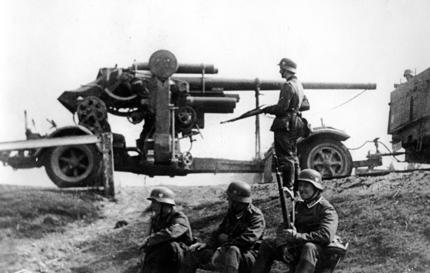 An 8.8 cm Flak 18 gun, supported by a Sonder Anhanger 201/202 carriage, is seen with German soldiers during the 1940 invasion of France. The carriage enhances the gun’s maneuverability, allowing it to keep pace with the rapid German advance. The soldiers’ readiness highlights the strategic use of this versatile weapon in anti-aircraft and ground roles. This scene captures a pivotal moment in Germany’s early World War II campaigns.