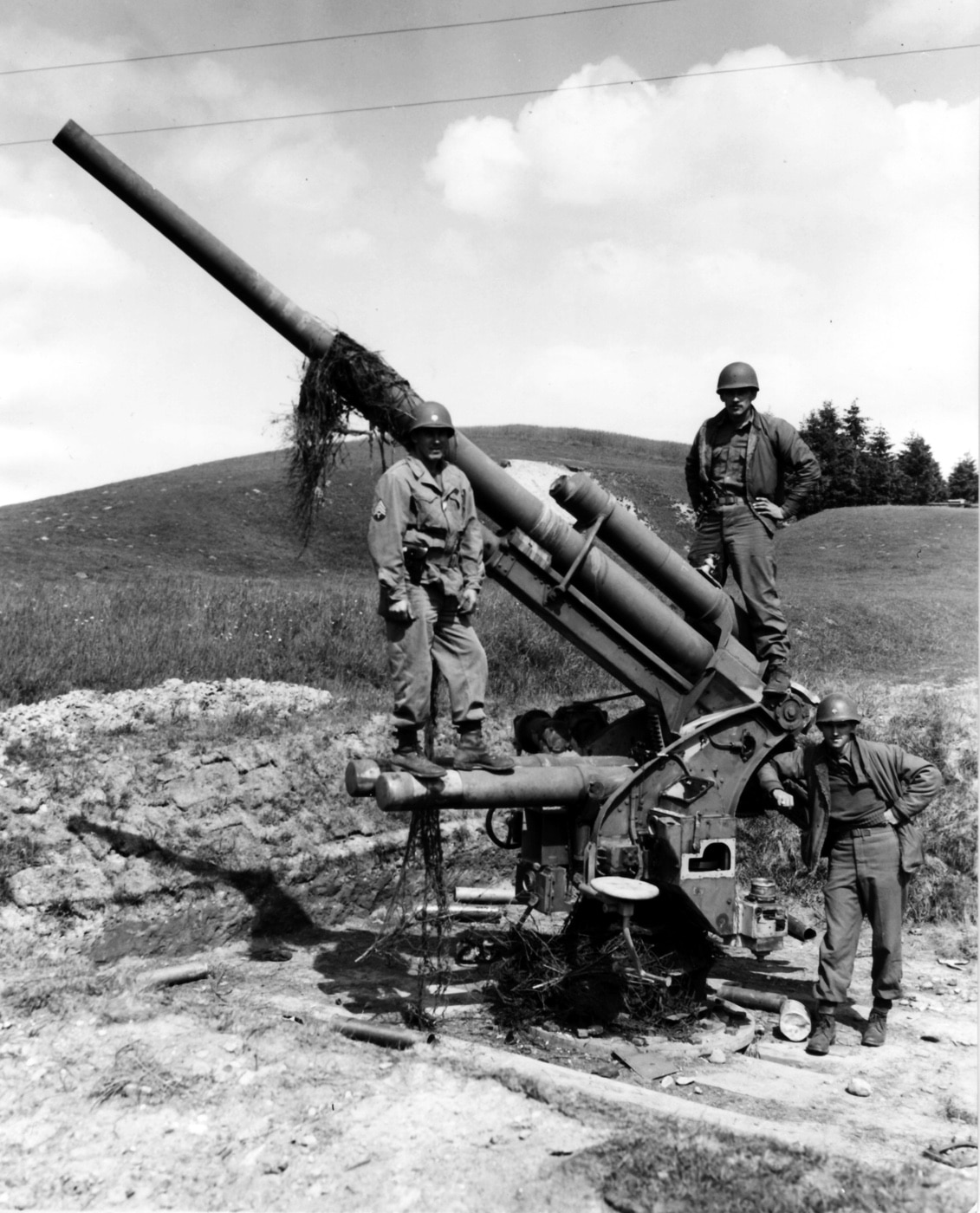 American GIs inspect a captured 88mm Flak gun in Augsburg, Germany, in May 1945 near the end of World War II. The imposing weapon, known for its dual role in anti-aircraft and anti-tank operations, stands as a symbol of German engineering. The soldiers examine the gun closely, reflecting their interest in its design and effectiveness. This moment captures the aftermath of the conflict as Allied forces secure German weapons and territory.