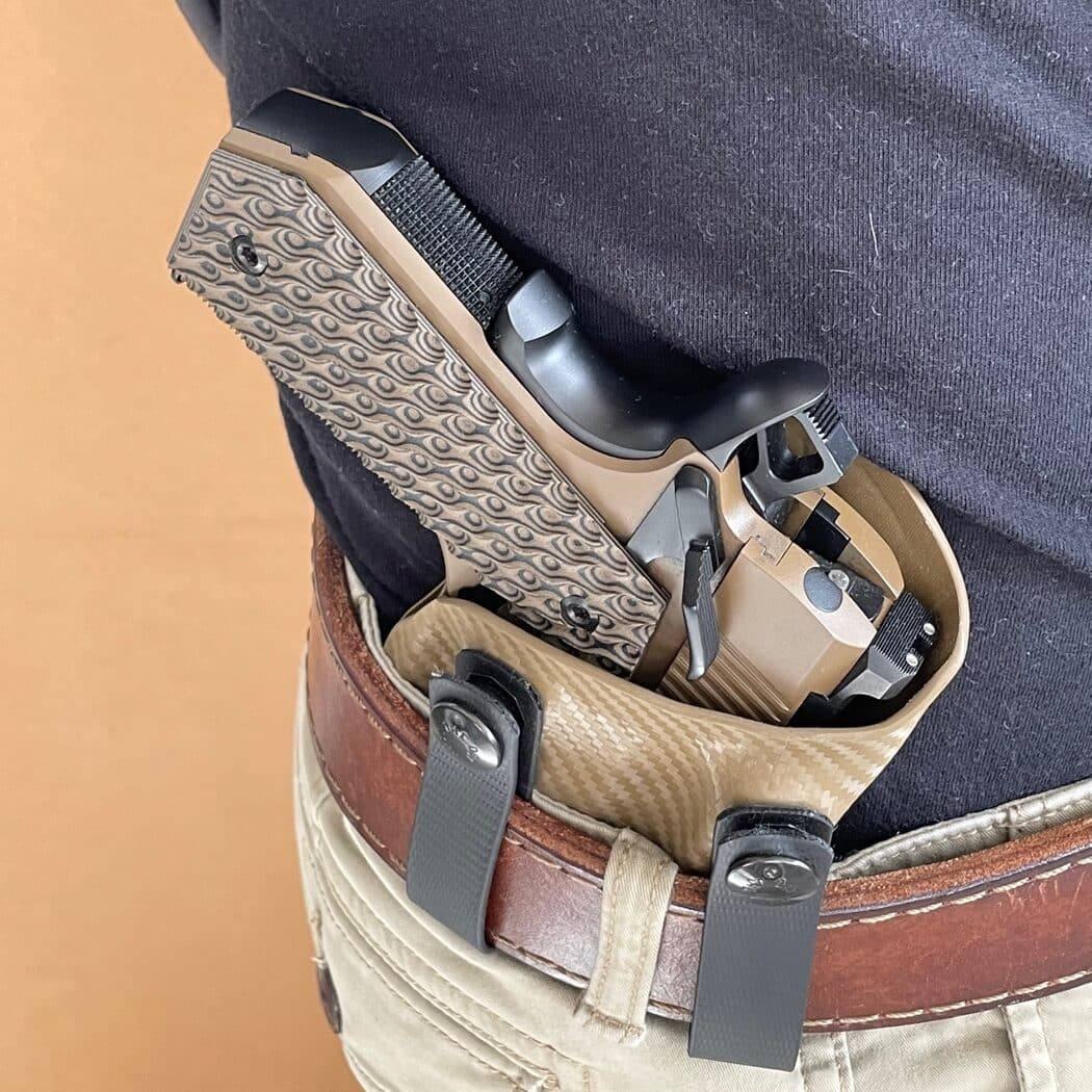 The author lifts his shirt to display a Springfield Armory 1911 pistol holstered in a Kydex IWB holster. The Carry Contour cut on the pistol grip is evident, showcasing its rounded edge that minimizes visible printing. The image emphasizes how the firearm remains concealed and comfortable when worn. This practical demonstration illustrates the benefits of the Carry Contour feature for concealed carry users.