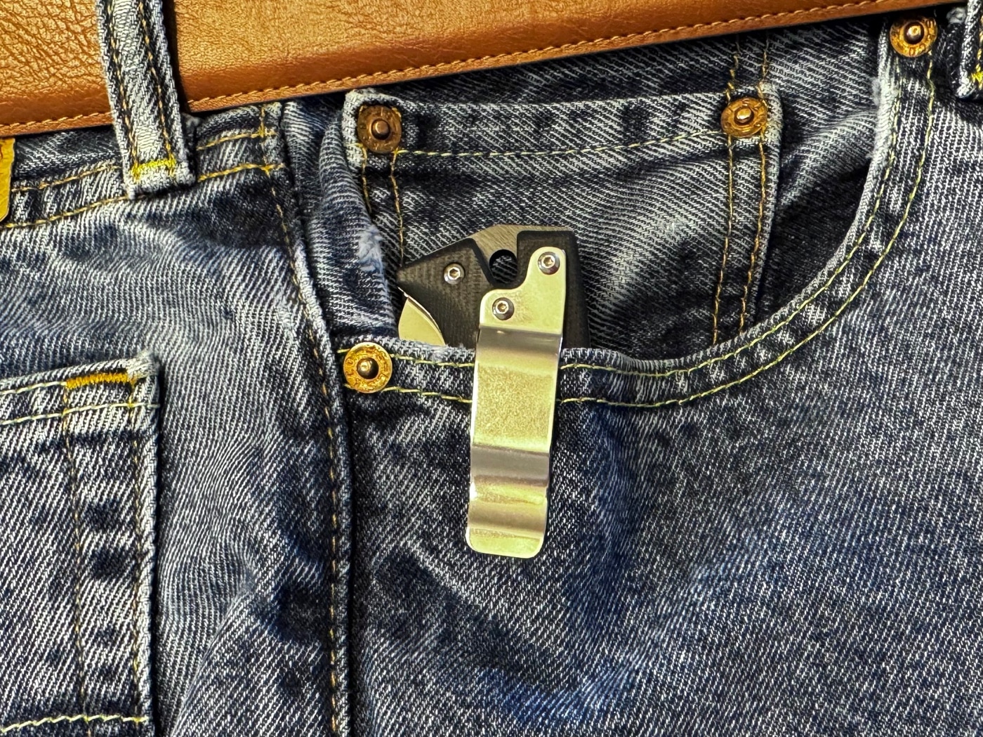 The Cold Steel AD-10 Tanto knife carried in a jeans pocket, with its wide, flat pocket clip visible. The clip keeps the knife securely in place while maintaining a discreet profile for everyday carry. Its ergonomic design ensures comfort and accessibility, even during active use. This Cold Steel AD-10 review discusses its handle design, portability, and pros and cons for EDC knife users.