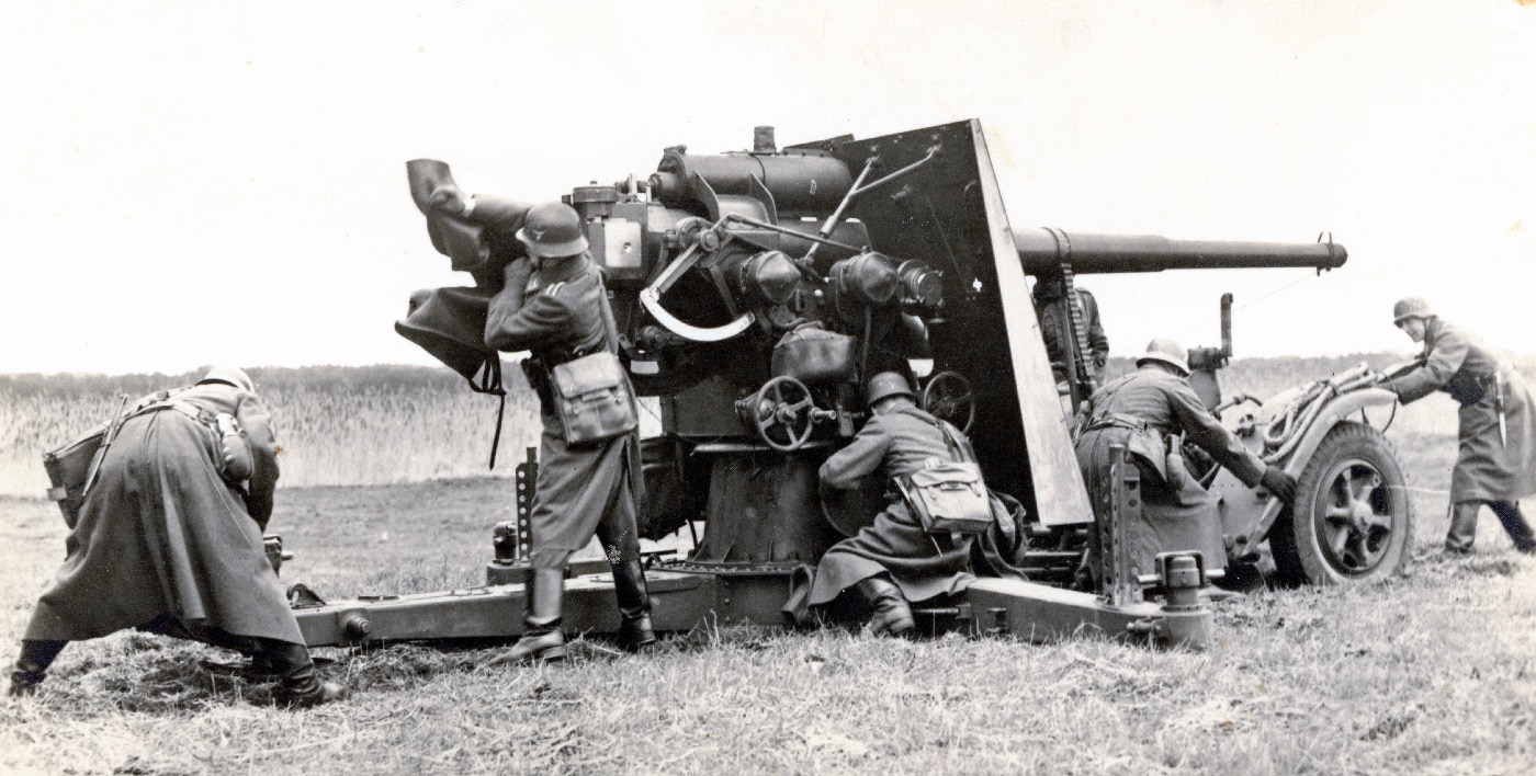 A German 8.8 cm Flak 18 anti-aircraft gun mounted on a specialized Sonder Anhanger 201/202 carriage with a cruciform platform for optimal deployment. The cruciform base allows the weapon to pivot and elevate effectively, enabling precise targeting of aerial and ground threats. The powerful Flak 18, renowned for its dual-purpose use, demonstrates the adaptability of German wartime artillery. This setup highlights its critical role in defensive and offensive operations during World War II.