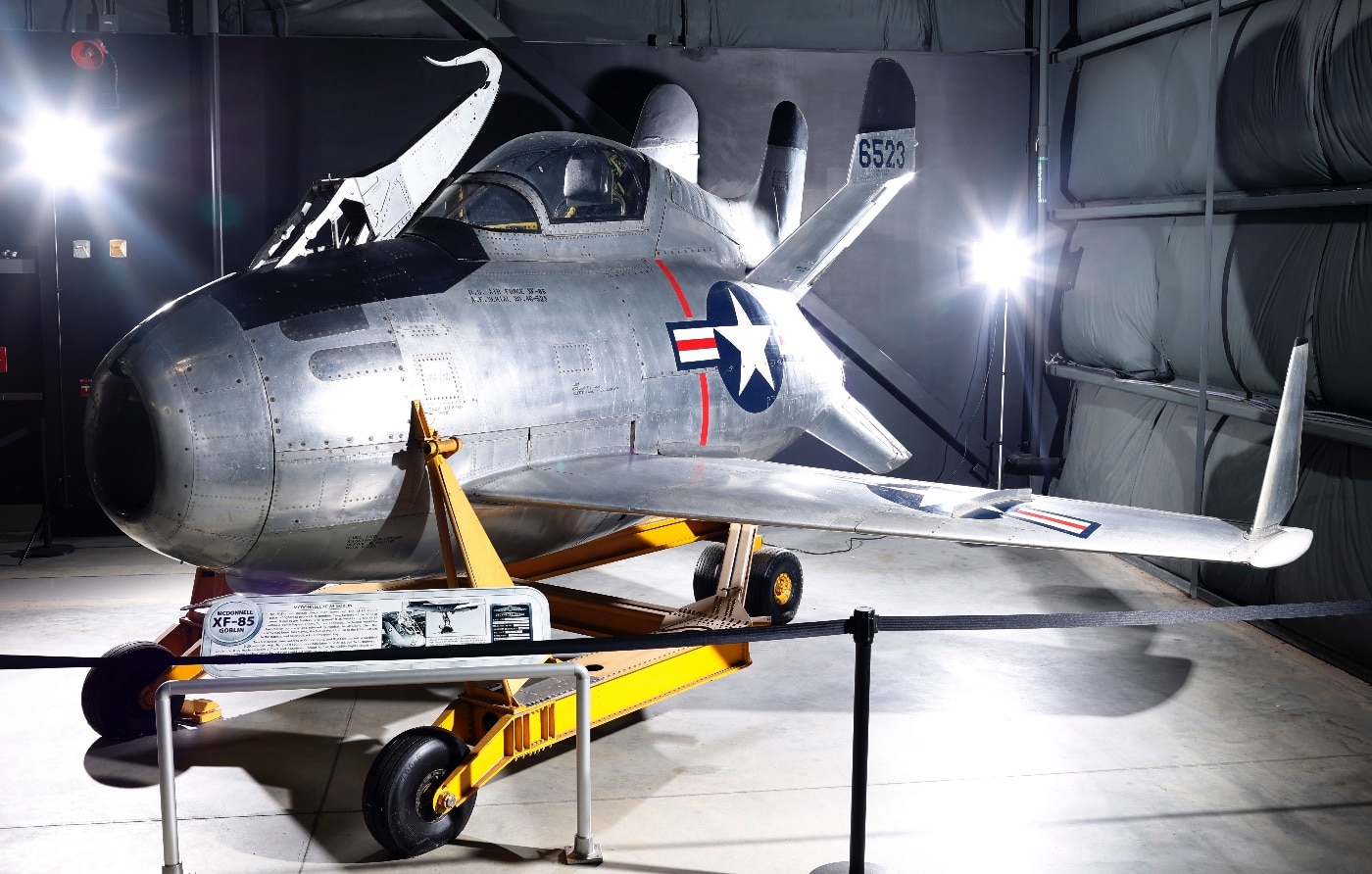 A preserved McDonnell XF-85 Goblin parasite fighter is showcased inside the National Museum of the Air Force. The aircraft is compact, with a rounded fuselage and short wings, reflecting its unique design as a deployable fighter for bombers. Positioned prominently, the Goblin serves as a historical example of experimental aviation technology from the late 1940s. Visitors can admire its innovative shape and engineering up close.