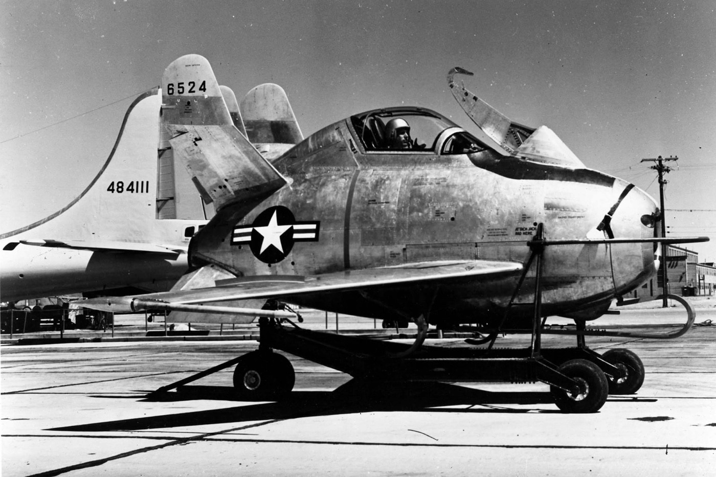 A pilot sits patiently in the small cockpit of the McDonnell XF-85 Goblin, preparing for a test flight. The Goblin, with its rounded fuselage and compact size, is awaiting attachment to a B-29 Superfortress for an experimental mission. The photo showcases the aircraft's tight workspace and the precision required for testing such advanced concepts. This moment reflects the ambitious attempts to innovate bomber defense in the late 1940s.