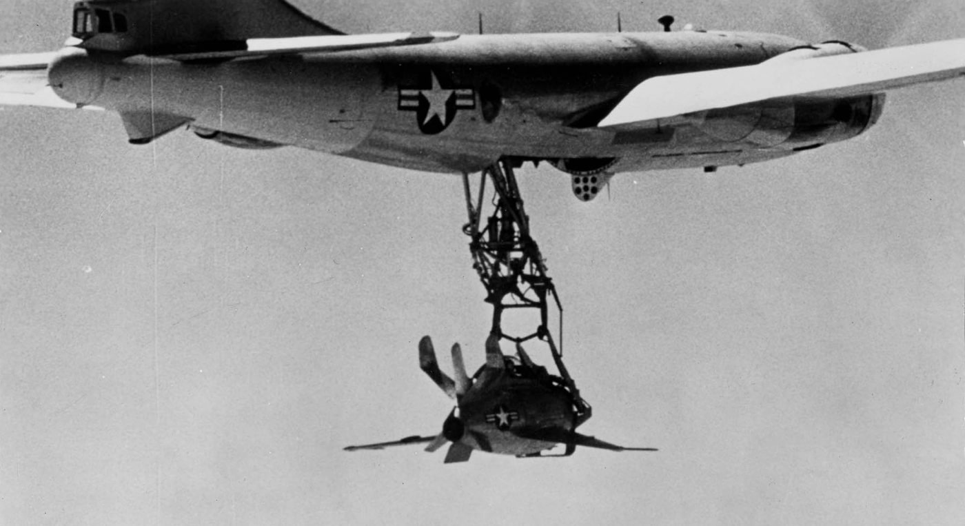 A historical image of the McDonnell XF-85 Goblin parasite fighter jet secured beneath a B-29 Superfortress bomber. The tiny, egg-shaped aircraft was built to be carried and launched mid-flight as a defense measure for bombers. Its unique, compact design reflects the innovation of late 1940s aviation technology. This image highlights the experimental vision of the U.S. Air Force to protect long-range bombers during missions.