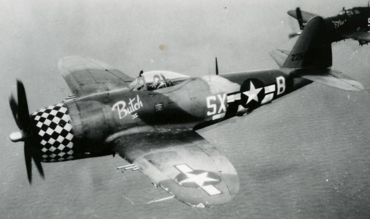 A P-47 Thunderbolt pilot from the 352nd Fighter Squadron is caught in a candid moment, glancing at the camera like he knows he’s the star of the show. The cockpit canopy sparkles, framing his “don’t mess with me” expression. It’s the kind of look that says, “Yes, I fly a Thunderbolt, and no, I don’t break a sweat.” Somewhere in the background, another pilot is probably saying, “How do I get my photo taken like that?”