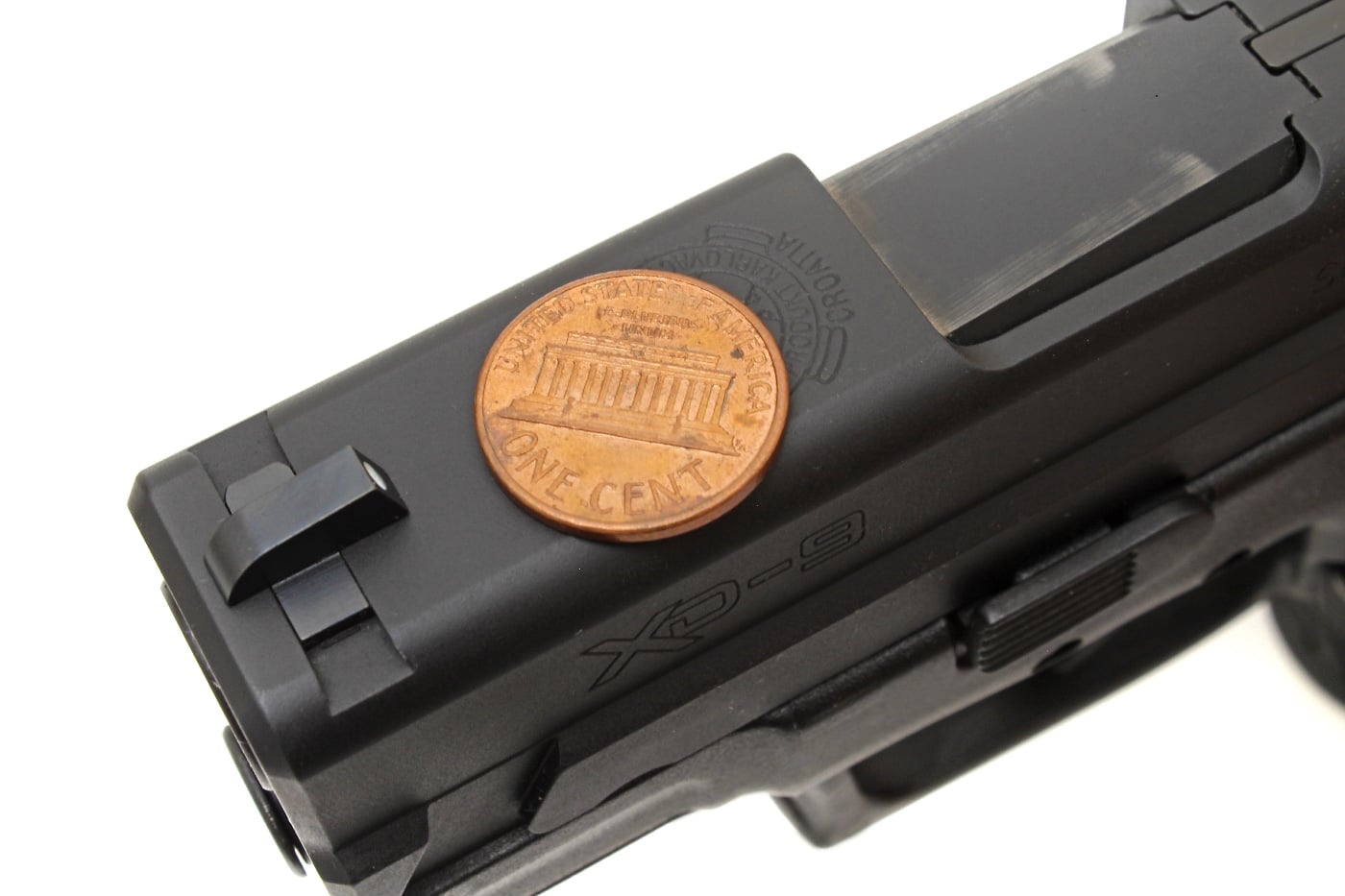 A Springfield Armory XD 9mm pistol with a penny carefully balanced on the slide during dry fire training. This technique helps shooters practice a smooth trigger pull without disturbing the sights. The penny remains steady, demonstrating precise trigger control and firearm handling skills. Dry fire exercises like this are essential for developing marksmanship without live ammunition.