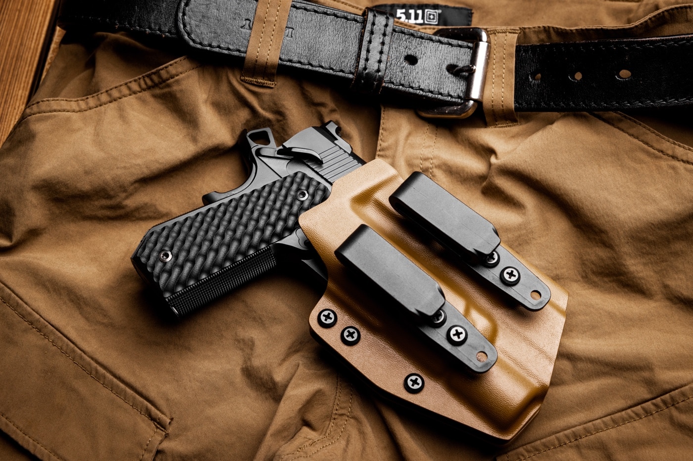 A Springfield Armory 1911 pistol with the Carry Contour cut is displayed inside a Kydex holster. Both the pistol and holster rest on a pair of 5.11 cargo pants, known for their tactical and practical design. The Carry Contour grip is visible, emphasizing the pistol's suitability for concealed carry. This arrangement showcases a combination of durable and functional gear tailored for everyday concealed carry needs.