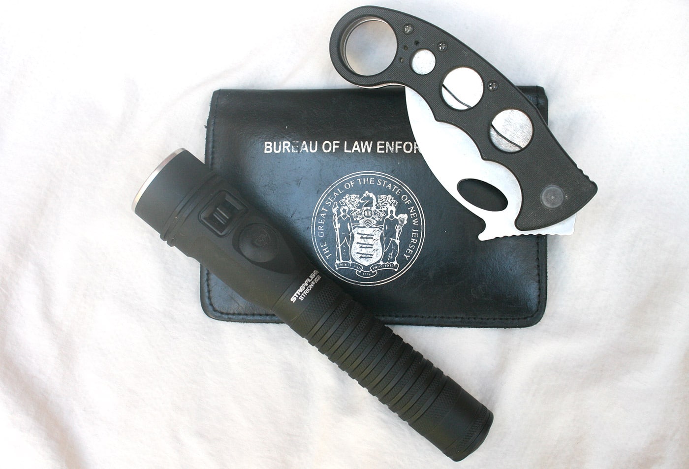 In this photo, the author shows us the Streamlight Strion 2020 flashlight with a folding knife and his police credentials. The purpose of the photo is to demonstrate how small the flashlight is. It is large enough to get your hand on but compact enough to slip easily into a pocket and be carried all day long.