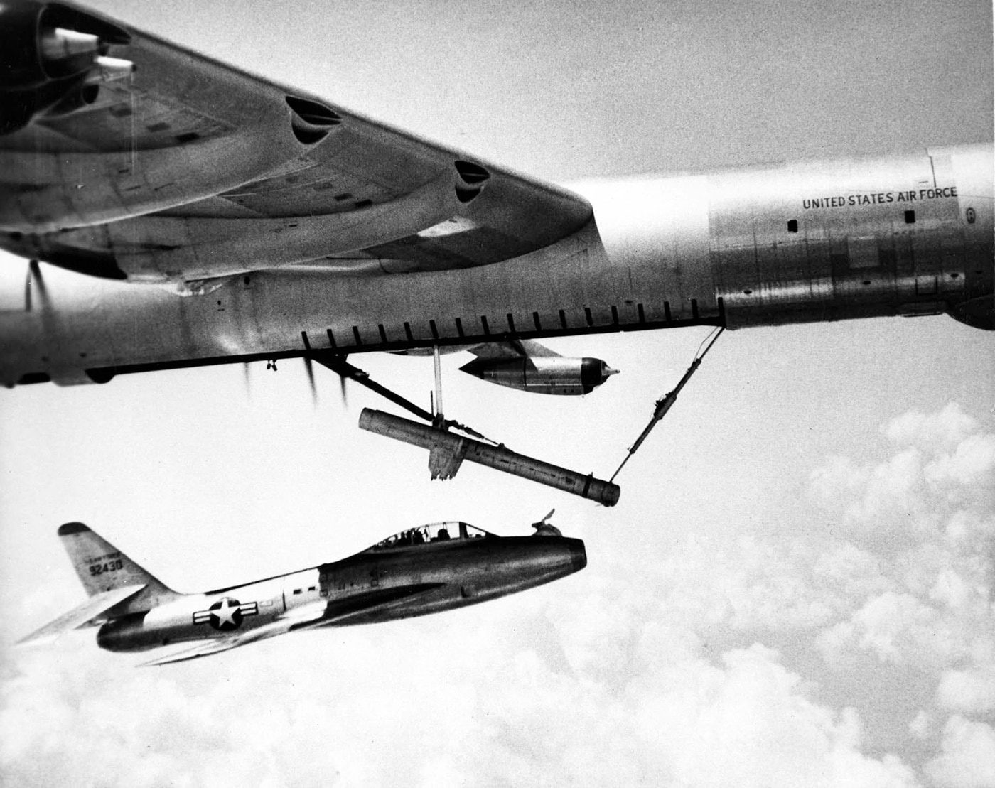 The YRF-84F fighter jet is shown flying directly underneath a B-36 Peacemaker bomber during a test mission. This experimental setup was part of a Cold War effort to test the feasibility of parasite fighters, small jets carried and deployed by large bombers. The sleek YRF-84F contrasts with the massive, imposing B-36 above it. The image captures a moment of aviation innovation as engineers sought to extend bomber protection capabilities over long ranges.