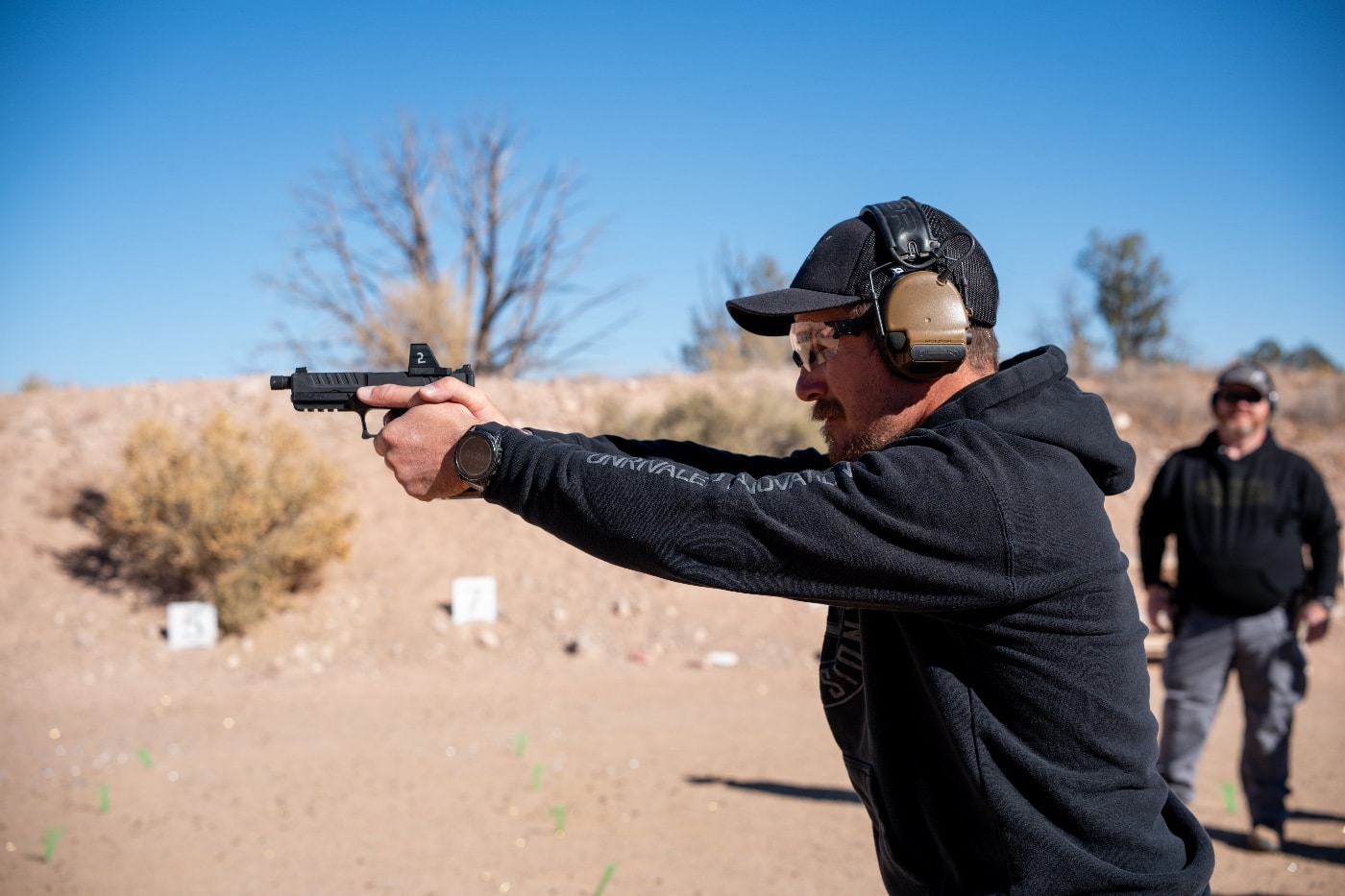 A student is captured mid-shoot on the Gunsite Academy range, firing a Springfield Armory Echelon pistol as part of an advanced shooting class. The student’s stance is steady, demonstrating focus and discipline while gripping the firearm. The pistol’s ergonomic design and precision are emphasized in this action shot. The backdrop includes steel targets and rugged terrain typical of Gunsite’s outdoor range. This photo highlights the hands-on training and practical skill development central to the Performance Pistol Symposium.