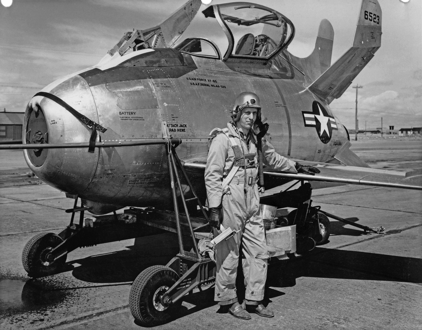 Test pilot Edwin Foresman Schoch is seen standing beside the McDonnell XF-85 Goblin at Edwards Air Force Base. Schoch was responsible for testing the parasite fighter, designed to be deployed mid-flight from bombers like the B-29. The compact size of the aircraft is evident next to the pilot, showcasing its unique design. This image reflects the courage and skill of test pilots involved in Cold War aviation experiments.