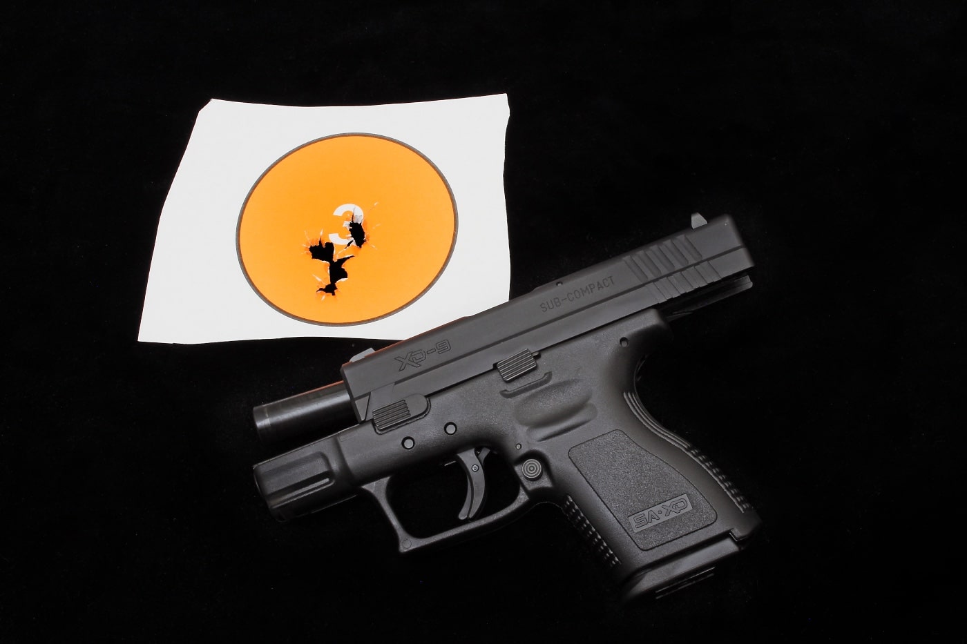 A Springfield Armory XD pistol displayed alongside a target showcasing a tight group of bullet holes, signifying accurate shooting. The impressive results highlight the importance of combining dry fire and live fire training for skill development. Even compact firearms like this 3-inch XD can achieve high precision with consistent practice. This demonstrates the value of a balanced training approach for marksmanship.