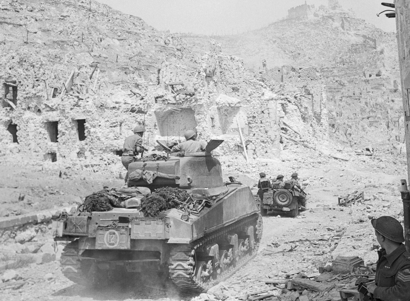 The 4th New Zealand Armoured Brigade enters the ruins of Monte Cassino Monastery following the Battle of Monte Cassino in 1944. A jeep and M4 Sherman tanks are visible amidst the rubble, emphasizing the extensive destruction of the historic site after prolonged combat and Allied bombing. The scene marks the brigade's significant contribution to the Allied breakthrough of the Gustav Line, a key victory in the Italian Campaign. The ruined monastery symbolizes the fierce resistance encountered and the high cost of the battle. This image highlights the pivotal role of New Zealand forces in securing the strategically vital position.