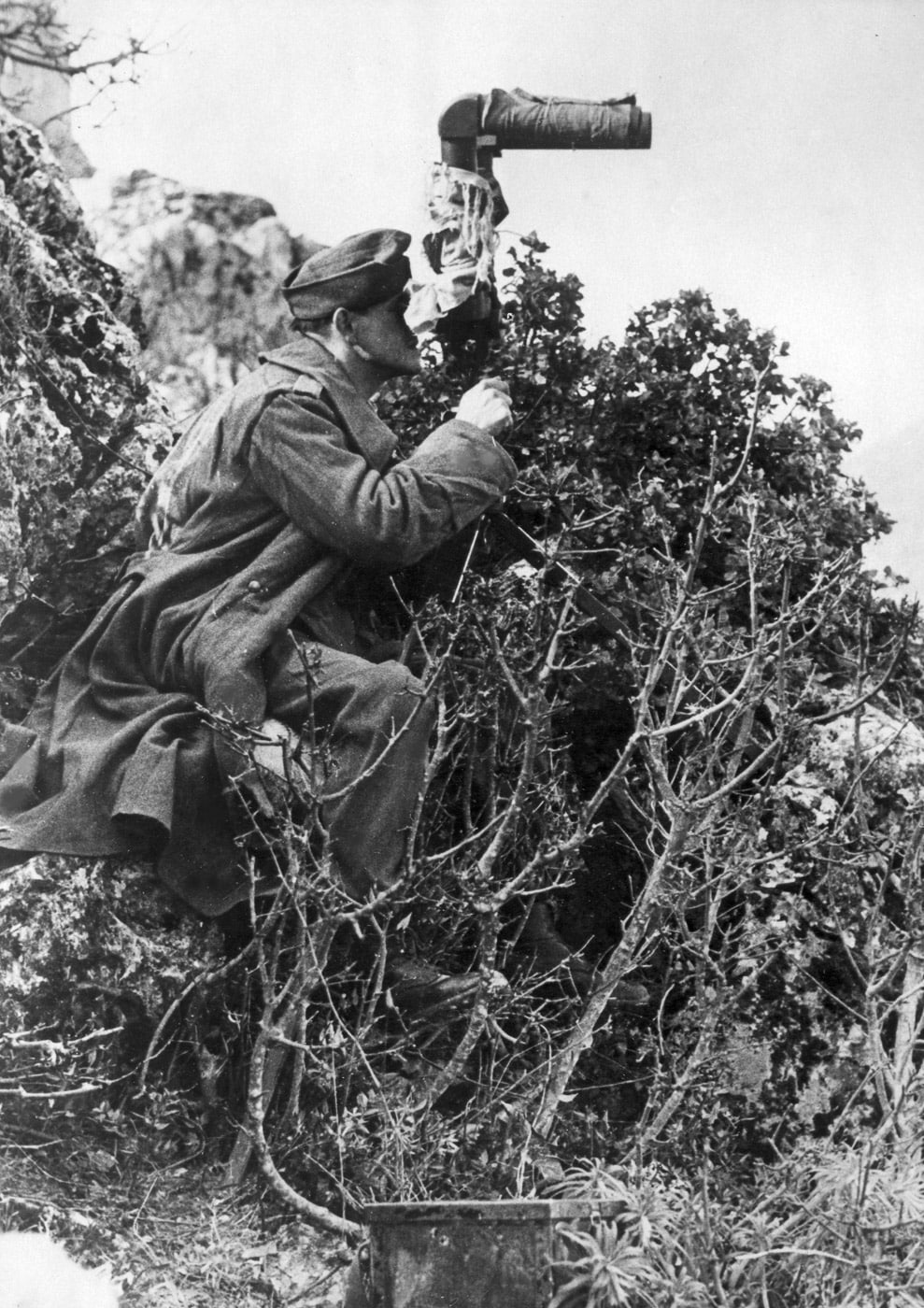 A German observer uses Scherenfernrohr SF14ZGi scissor binoculars, equipped with sun visors and camouflaged with fabric, during the Battle of Monte Cassino. Positioned on the slope of Monte Cassino hill, the observer utilizes the specialized binoculars to survey Allied movements while remaining concealed. The Scherenfernrohr, a critical tool for artillery and battlefield reconnaissance, allowed for precise and covert observations in challenging combat environments. The camouflage fabric blends with the rugged terrain, reflecting the strategic use of stealth by German forces defending the Gustav Line. This image illustrates the high level of preparation and technology employed in the German defensive effort. It underscores the intense observational and tactical challenges during the prolonged battle in the Italian Campaign.