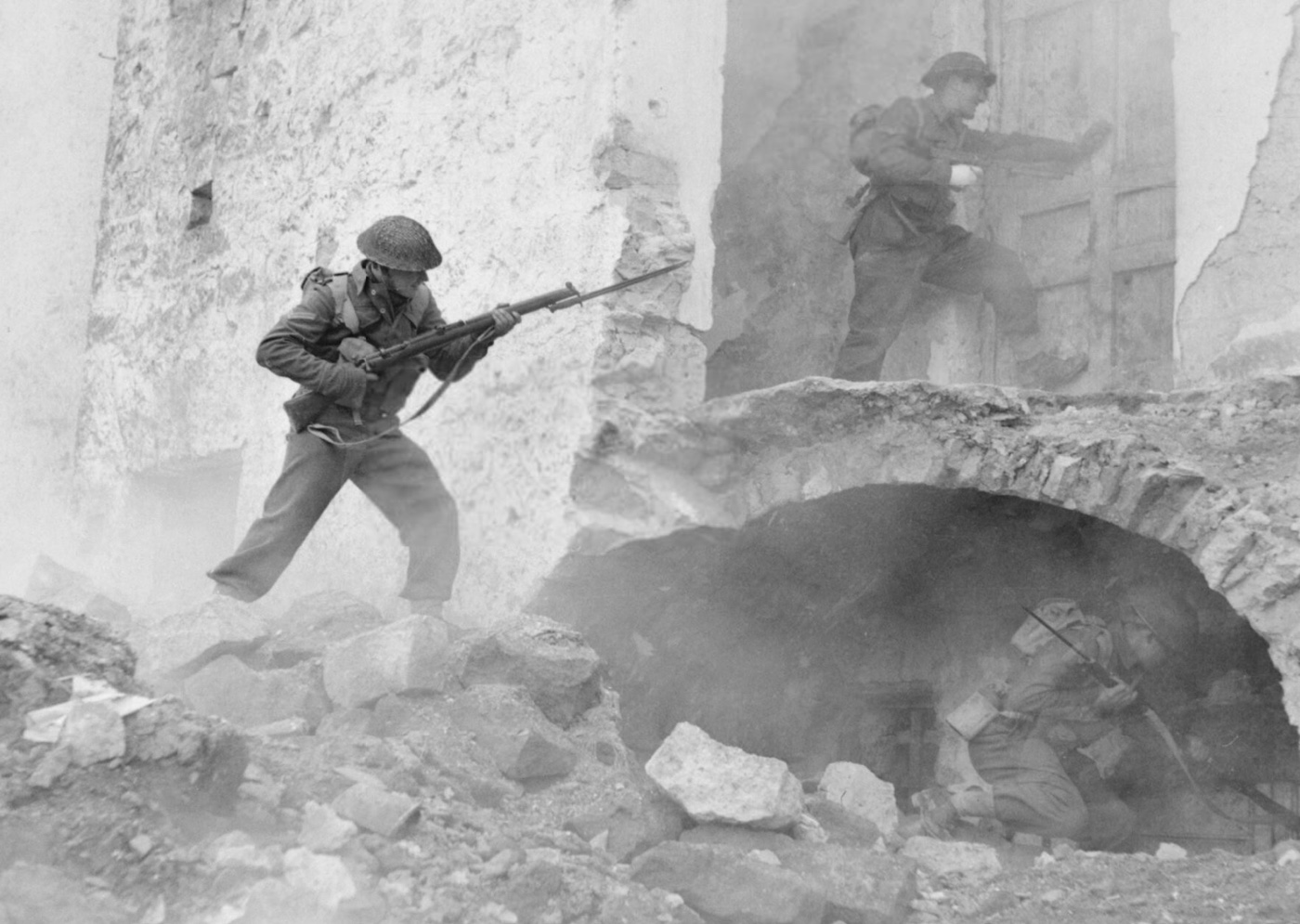 British infantry soldiers are shown clearing buildings in the town of Cassino, Italy, during the Battle of Monte Cassino on 24 March 1944. The soldiers move cautiously through the rubble-strewn streets, reflecting the fierce urban combat that characterized this phase of the battle. Heavily damaged buildings dominate the scene, highlighting the extensive destruction caused by artillery and aerial bombardments. The operation was part of the Allied effort to dislodge German defenders from fortified positions along the Gustav Line. This decisive battle was critical to the eventual Allied breakthrough in the Italian Campaign. The image conveys the intensity and challenges of urban warfare in World War II.