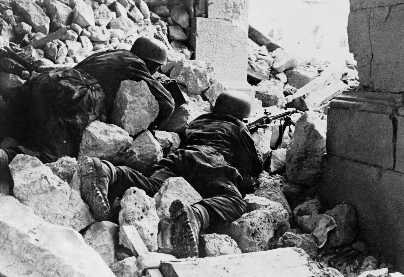 German Fallschirmjäger paratroopers are positioned within the ruins of Monte Cassino Abbey during the Battle of Monte Cassino, operating an MG42 machine gun. The soldiers lie among the rubble, taking advantage of the abbey's devastated structure for cover while defending their position on the Gustav Line. The MG42, known for its high rate of fire, was a formidable weapon against advancing Allied forces. The scene reflects the intense combat and strategic use of the abbey as a stronghold despite its destruction by Allied bombing. This image underscores the determination and resourcefulness of German defenders during the prolonged and bloody battle. It highlights the Abbey's transformation from a historic site to a battleground in the Italian Campaign.