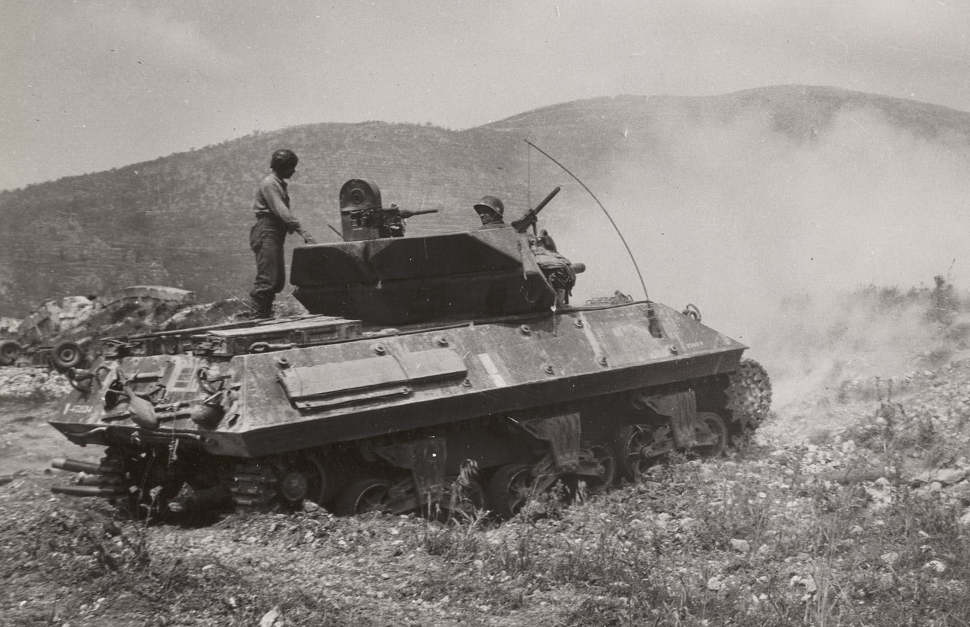 An M10 tank destroyer, manned by the French crew of an Algerian division, fires at German positions during the Battle of Monte Cassino in the Castleforte area. The scene captures the decisive role of Allied armored units in overcoming German defenses along the Gustav Line. The M10, positioned amidst rugged terrain, demonstrates the firepower and versatility used to support ground troops in the intense combat. The involvement of Algerian forces highlights the diverse makeup of the Allied effort during the Italian Campaign. This image reflects the coordination and determination required to break through fortified German strongholds at Monte Cassino.