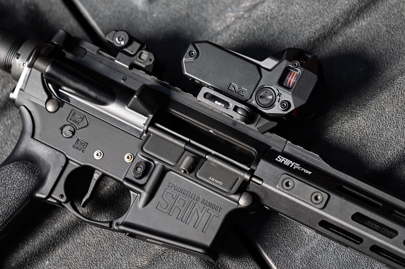 A laydown product photo showcasing the Meprolight M22 red dot sight mounted on the Picatinny rail of a Springfield Armory SAINT rifle. The optic’s quick detach (QD) mounting system is prominently displayed, emphasizing its ease of use. The matte black finish of the sight complements the rifle, showcasing a sleek and modern aesthetic. The compact design allows for compatibility with additional attachments, such as magnifiers or night vision devices. This image highlights the practicality and durability of the QD system for shooters needing reliable, fast adjustments in dynamic situations.