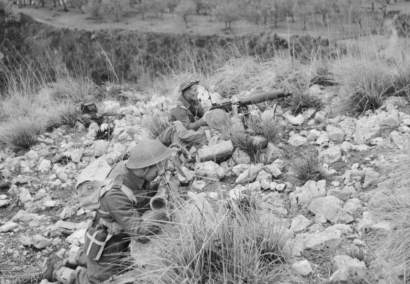 A Vickers machine gun crew from the 2nd New Zealand Division operates their weapon during attacks on German positions at Monte Cassino. The soldiers are focused on their task, positioned behind the gun as they provide suppressing fire to support the Allied advance against the heavily fortified Gustav Line. The rugged terrain and rubble in the background highlight the challenging conditions of the battle. The Vickers machine gun, known for its reliability, played a crucial role in the prolonged and intense fighting at Monte Cassino. This image illustrates the dedication and teamwork of the New Zealand forces during a pivotal moment in the Italian Campaign.