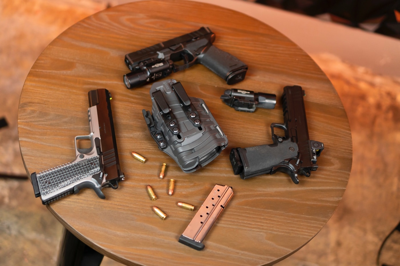 The PHLster Floodlight2 holster is displayed alongside an assortment of pistols, highlighting its universal fit for light-bearing firearms. The holster's innovative design indexes retention off the weapon-mounted light, making it compatible with multiple models, including compact and full-size handguns. Pistols in the image are equipped with accessories such as red dot optics and suppressor-height sights, showcasing the holster’s adaptability. The wave-textured ComfortScape body ensures comfort during concealed carry by enhancing airflow and reducing pressure points. The open-ended design accommodates features like threaded barrels and compensators. Sturdy belt clips are visible, ensuring secure attachment for inside-the-waistband carry. This image emphasizes the Floodlight2’s versatility and practicality for firearm owners who need a single holster for multiple pistols.