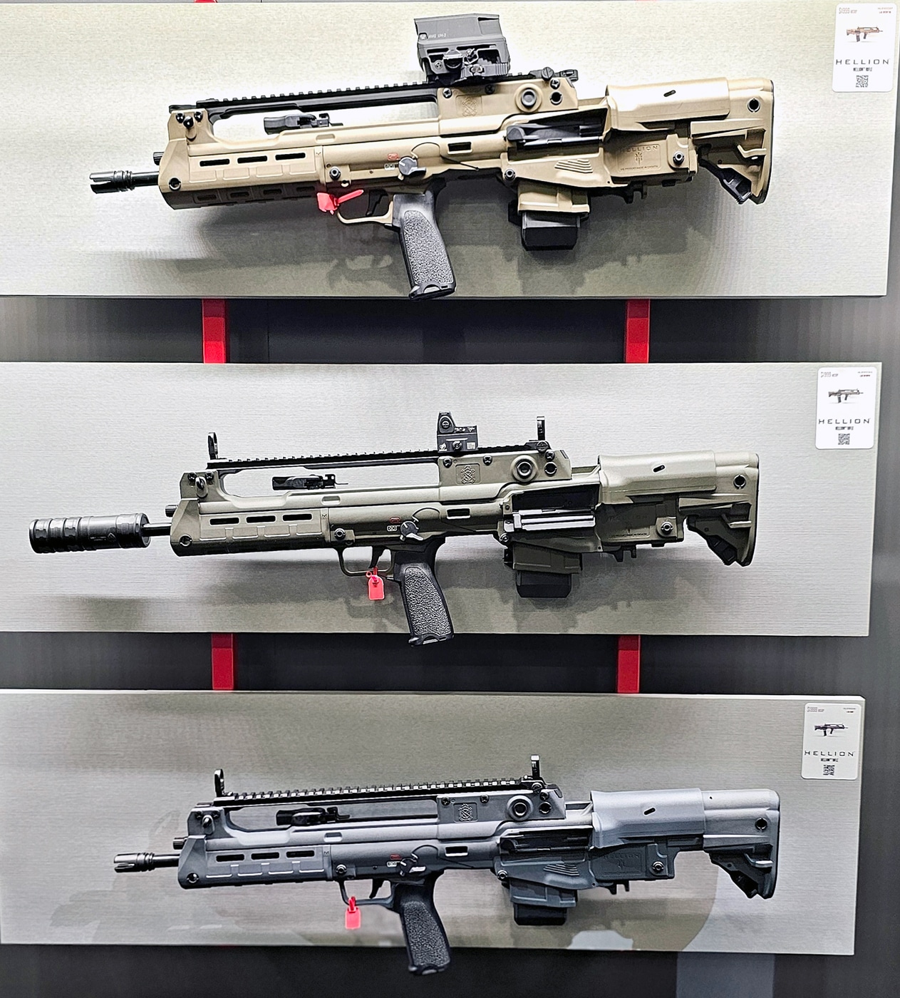 A row of Springfield Armory Hellion rifles is displayed prominently at the 2025 SHOT Show, featuring an array of new color finishes. The lineup includes OD Green, Flat Dark Earth (FDE), and Grey, each adding a distinct aesthetic to the already striking design of the Hellion. The rifles are neatly arranged on an illuminated rack, with detailed signage describing their features, including the bullpup configuration and adaptable controls. Attendees can be seen in the background, engaging with other firearm displays and chatting with Springfield representatives. The new colors highlight the Hellion’s versatility and modern appeal, catering to shooters with varied preferences. The lighting in the booth enhances the texture and finish of each rifle, emphasizing their durability and sleek profiles. This presentation underscores Springfield Armory’s commitment to offering functional firearms with a touch of personal style.