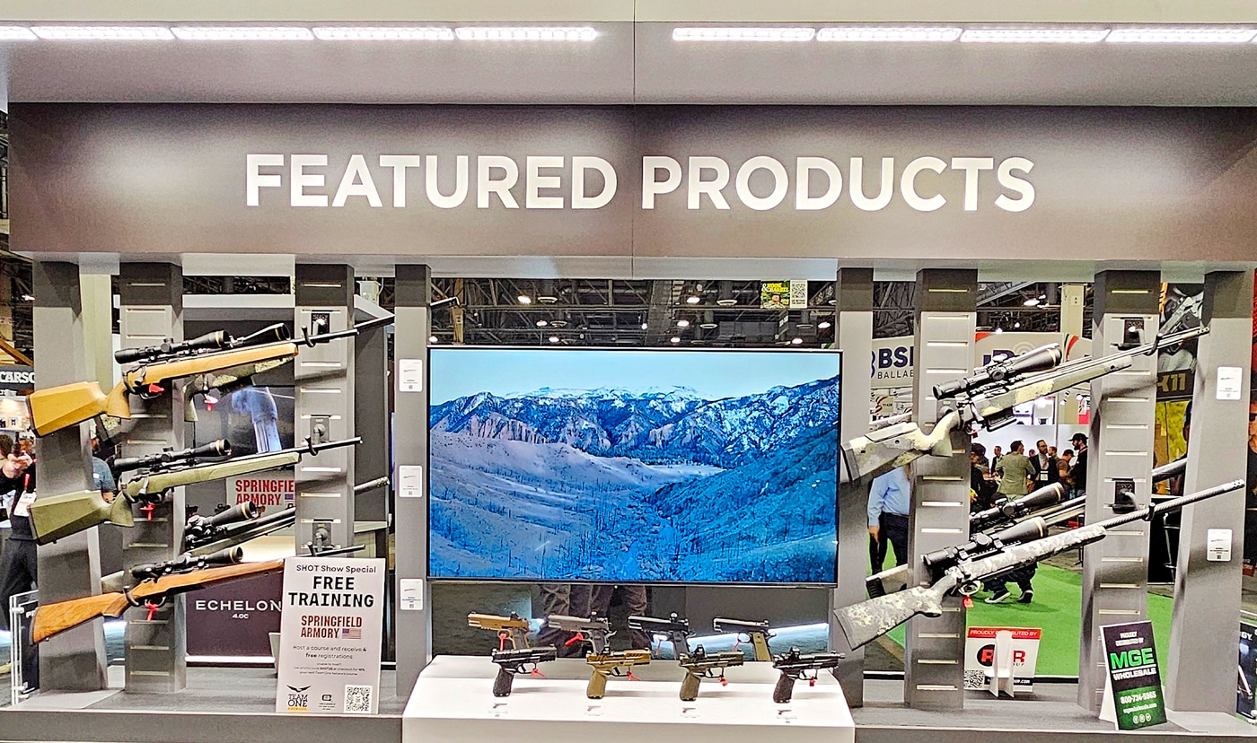 The featured products area at Springfield Armory’s exhibit booth, highlighting a curated selection of rifles and pistols for attendees at the 2025 SHOT Show. The rifles are mounted against a branded wall, including long-range models with precision stocks and shorter tactical variants. Pistols are displayed on freestanding pedestals, offering easy access for visitors to handle and examine the designs up close. The area is brightly lit with Springfield Armory logos and product information strategically placed to catch the eye. The booth is filled with attendees engaging with staff and exploring Springfield’s diverse lineup of firearms. This section serves as the focal point of the booth, showcasing the company’s innovations and commitment to excellence in firearm design.