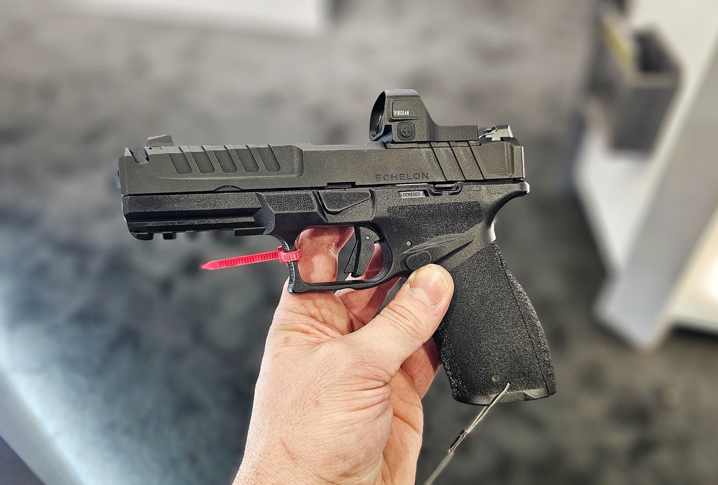 The author holds a Springfield Armory Echelon Compact pistol equipped with a Vortex red dot sight during the 2025 SHOT Show. The firearm features a compact frame and a 4.5-inch barrel, designed for versatility and ease of carry. The red dot sight is mounted on the pistol’s optics-ready slide, showcasing the adaptability of Springfield’s variable optics interface system. Bright lighting in the booth enhances the pistol’s clean lines and durable finish, while the Vortex sight adds a layer of precision shooting capability. In the background, attendees explore Springfield’s extensive exhibit, filled with various rifles, pistols, and displays. The author’s poised presentation emphasizes the pistol’s balance of innovation and practicality. This moment captures the excitement of Springfield’s cutting-edge offerings at the event.