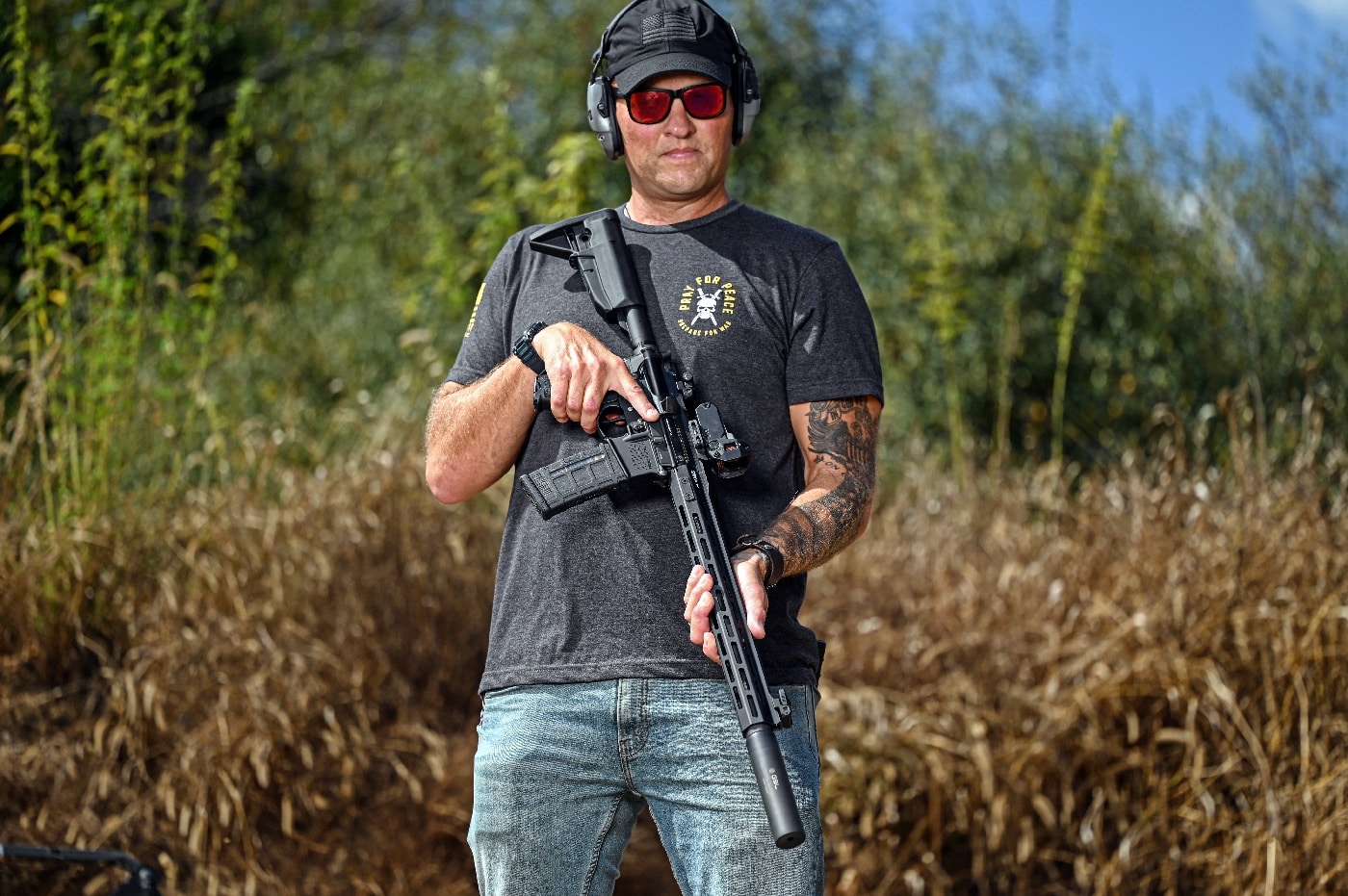 A photo of the author standing on a shooting range, holding a Springfield Armory SAINT rifle outfitted with the Meprolight M22 red dot sight. The rifle is prominently displayed, with the optic clearly mounted on its Picatinny rail. The author's stance and setting emphasize the practical testing of the optic in a live-fire environment. Bright outdoor lighting highlights the sleek design of the optic and its integration with the rifle. The image conveys confidence and showcases the usability of the Meprolight M22 in field conditions.