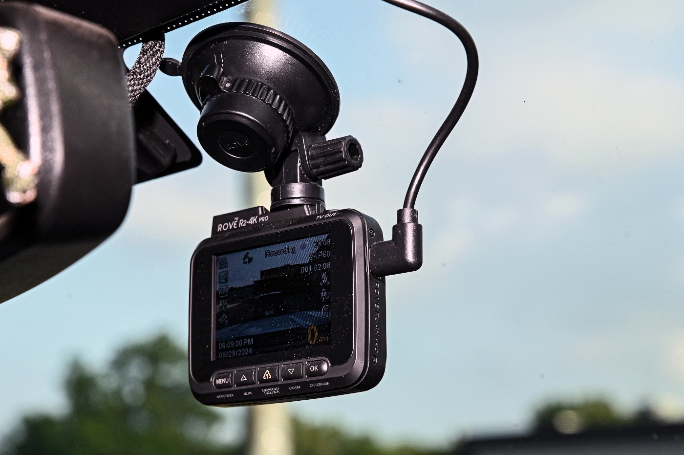 A close-up view of a dash cam securely mounted on a car windshield, ready to record the road ahead. The dash cam is sleek and modern, emphasizing its role as a critical safety tool in documenting incidents, such as carjackings or traffic collisions. The camera faces outward, ensuring a wide field of view to capture potential attackers or unusual behavior in surrounding vehicles. The interior of the car appears clean and organized, showcasing attention to safety and preparedness. This device offers an added layer of protection for drivers who may need clear evidence in the aftermath of a dangerous encounter. The background reveals an urban environment, further highlighting its use in high-traffic or potentially risky areas. This image emphasizes the importance of technology in personal security and legal protection.