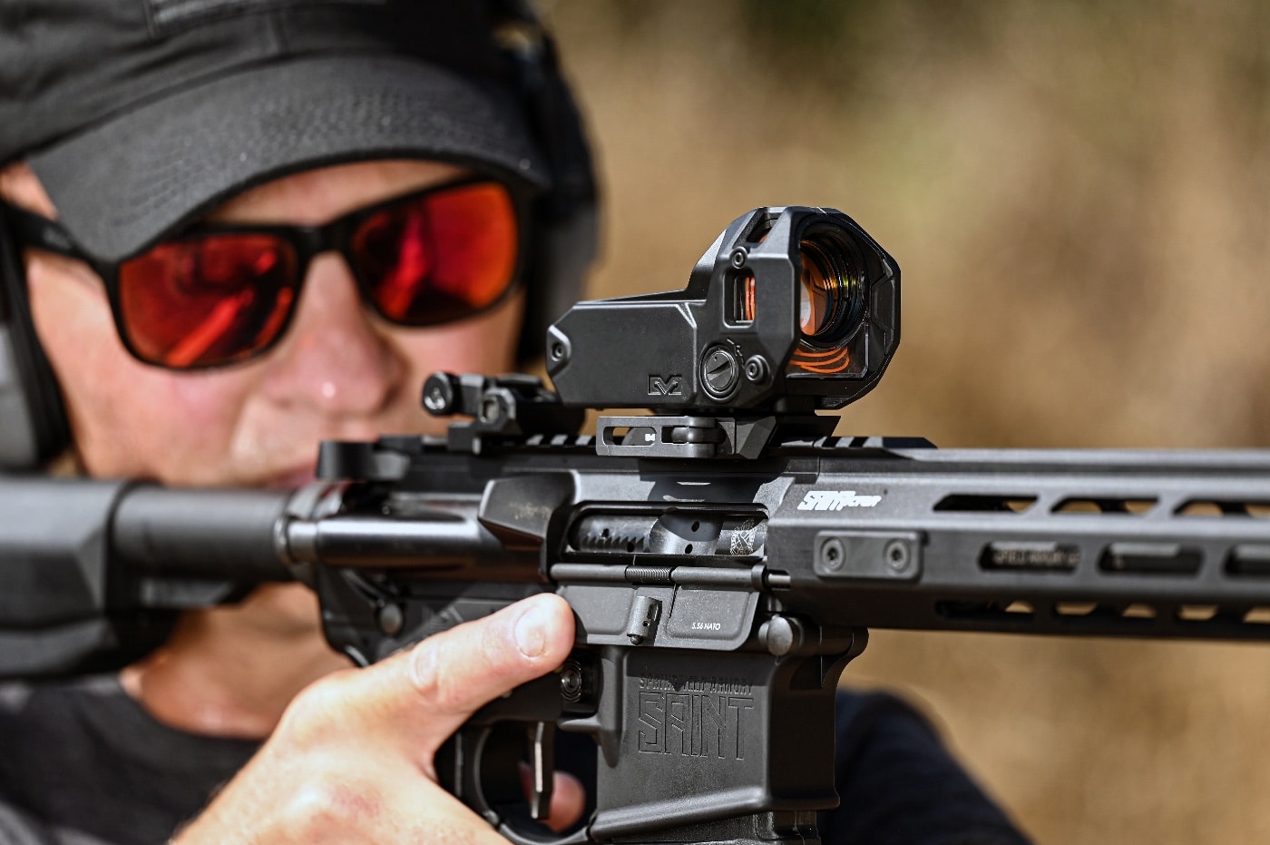 The author is seen aiming a Springfield Armory SAINT rifle equipped with the Meprolight M22 red dot sight. The fiber optic cables surrounding the optic’s housing are clearly visible, gathering ambient light to illuminate the reticle. The rifle is firmly supported, with the author focusing intently on a distant target. The self-illuminating optic eliminates the need for batteries, relying on fiber optics and tritium for all lighting conditions. This image captures the precision and reliability of the M22 during live-fire testing on a shooting range.