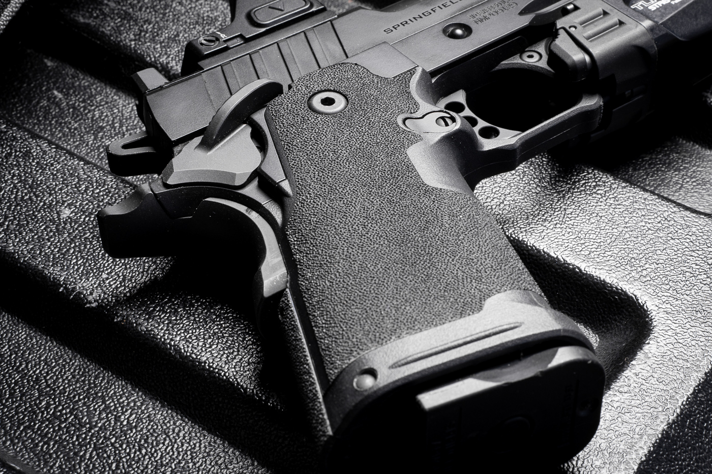 A detailed close-up of the grip on the Springfield Armory 1911 DS Prodigy Compact pistol. The Adaptive Grip Texture provides a tactile surface that becomes grippier as more pressure is applied, ensuring a secure hold during firing. The polymer frame is ergonomically shaped to fit comfortably in the hand without causing irritation, even during extended use. The grip design balances functionality with comfort, making it ideal for concealed carry. This image emphasizes the craftsmanship and practicality of the Prodigy Compact’s grip.