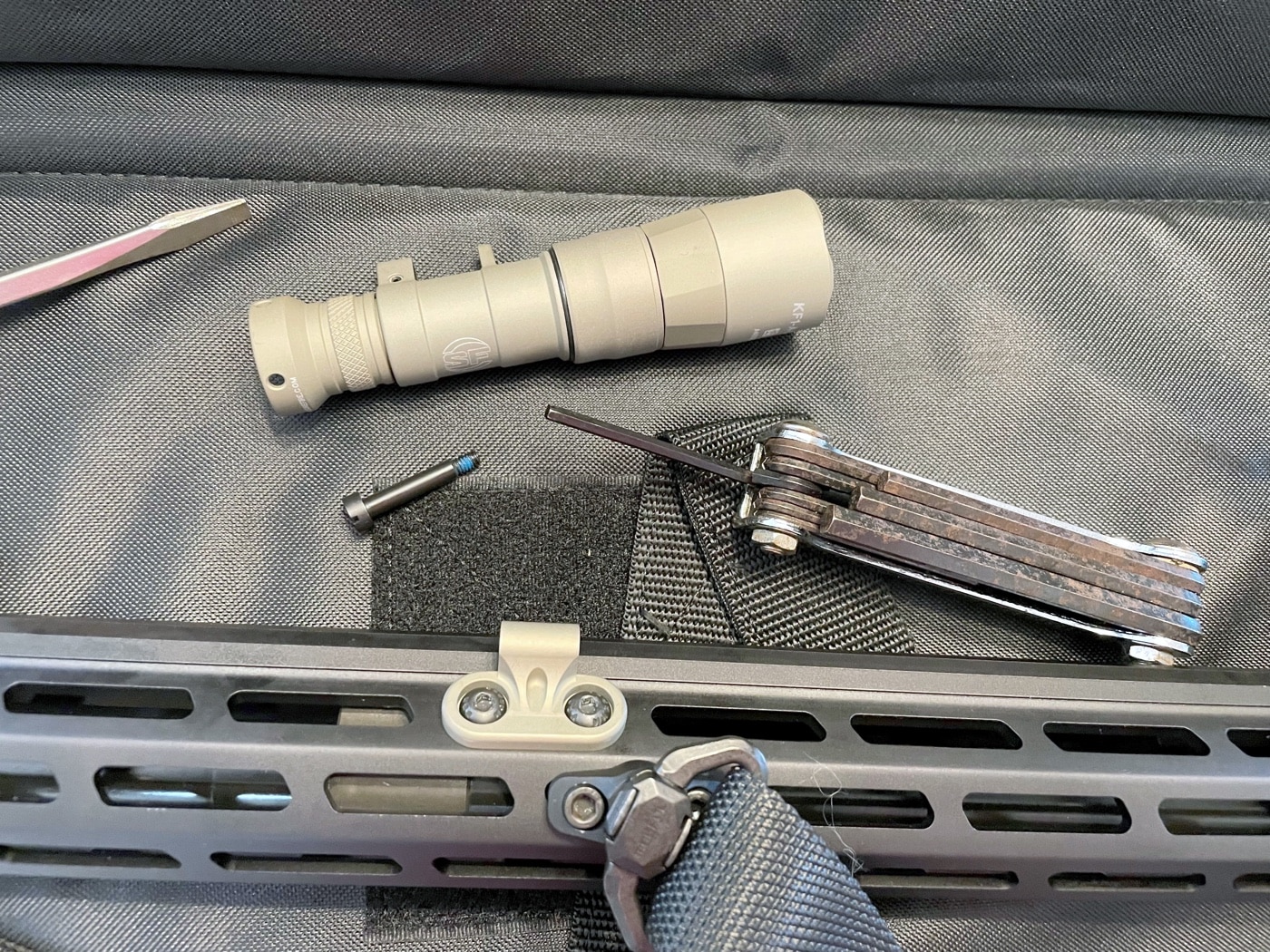 A collection of tools and parts used to mount the SureFire Mini Scout Pro flashlight to a rifle. The setup includes a slotted screwdriver, an Allen wrench, and the low-profile mounting hardware provided with the flashlight. The tools are neatly arranged, reflecting the simplicity of the installation process. This image highlights the ease with which users can attach the flashlight to MIL-STD-1913 or M-LOK rails. The straightforward nature of the assembly emphasizes the Mini Scout Pro’s practical and accessible design for all skill levels.