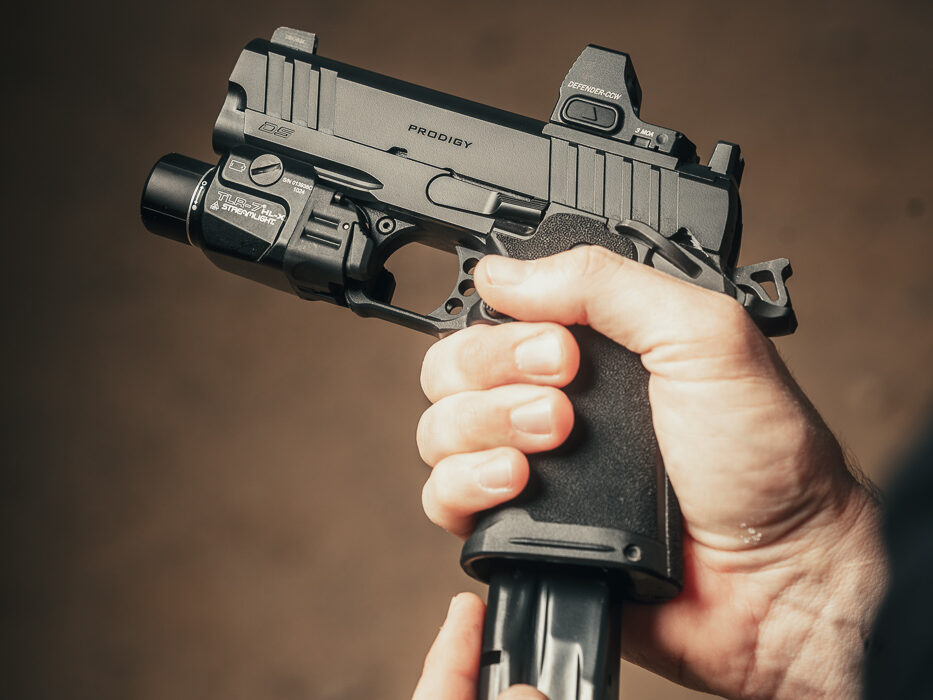 A photo of the author in the process of reloading the Springfield Armory 1911 DS Prodigy Compact pistol with a 3.5-inch barrel. The author holds the pistol in their dominant hand while inserting a fresh magazine with the other, demonstrating the pistol’s ergonomic and intuitive controls. The polymer grip’s Adaptive Grip Texture is clearly visible, providing a secure hold. The red dot sight and weapon light on the pistol highlight its defensive readiness. The scene emphasizes the ease and speed of reloading, even during dynamic use.