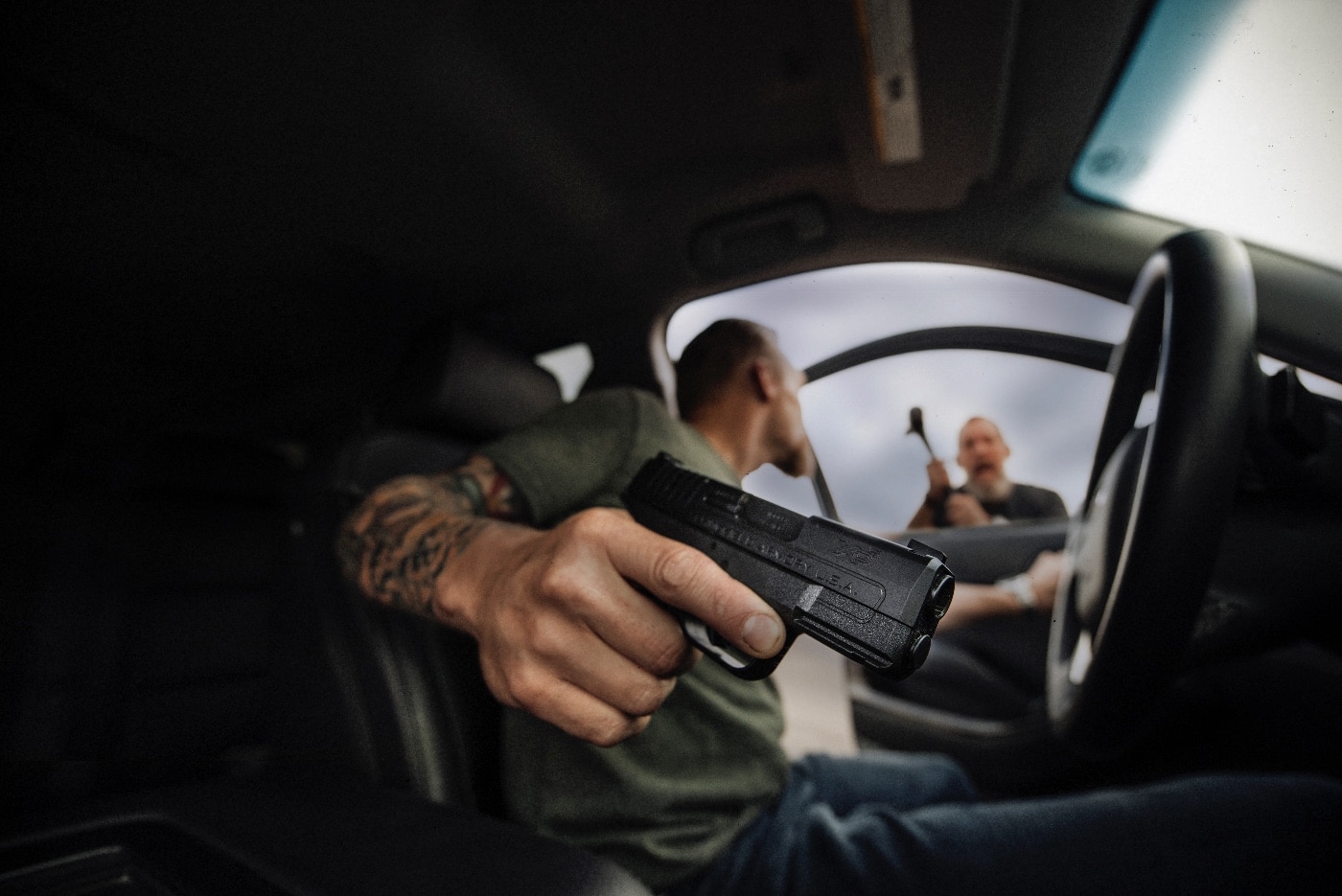 A man sits inside his truck, urgently drawing his Springfield Armory Echelon pistol as an attacker runs toward him holding a crowbar. The attacker, dressed in dark clothing, appears aggressive and focused on the vehicle. The truck's interior shows a calm but prepared driver responding to the unfolding threat. The attacker’s raised crowbar underscores the immediacy and danger of the situation. The urban background with surrounding traffic adds realism, demonstrating that such threats can occur unexpectedly in populated areas. The scene highlights the critical role of self-defense and situational awareness in responding to life-threatening encounters. The image emphasizes the confined nature of the truck, showing the challenge of drawing and aiming a firearm in tight quarters.