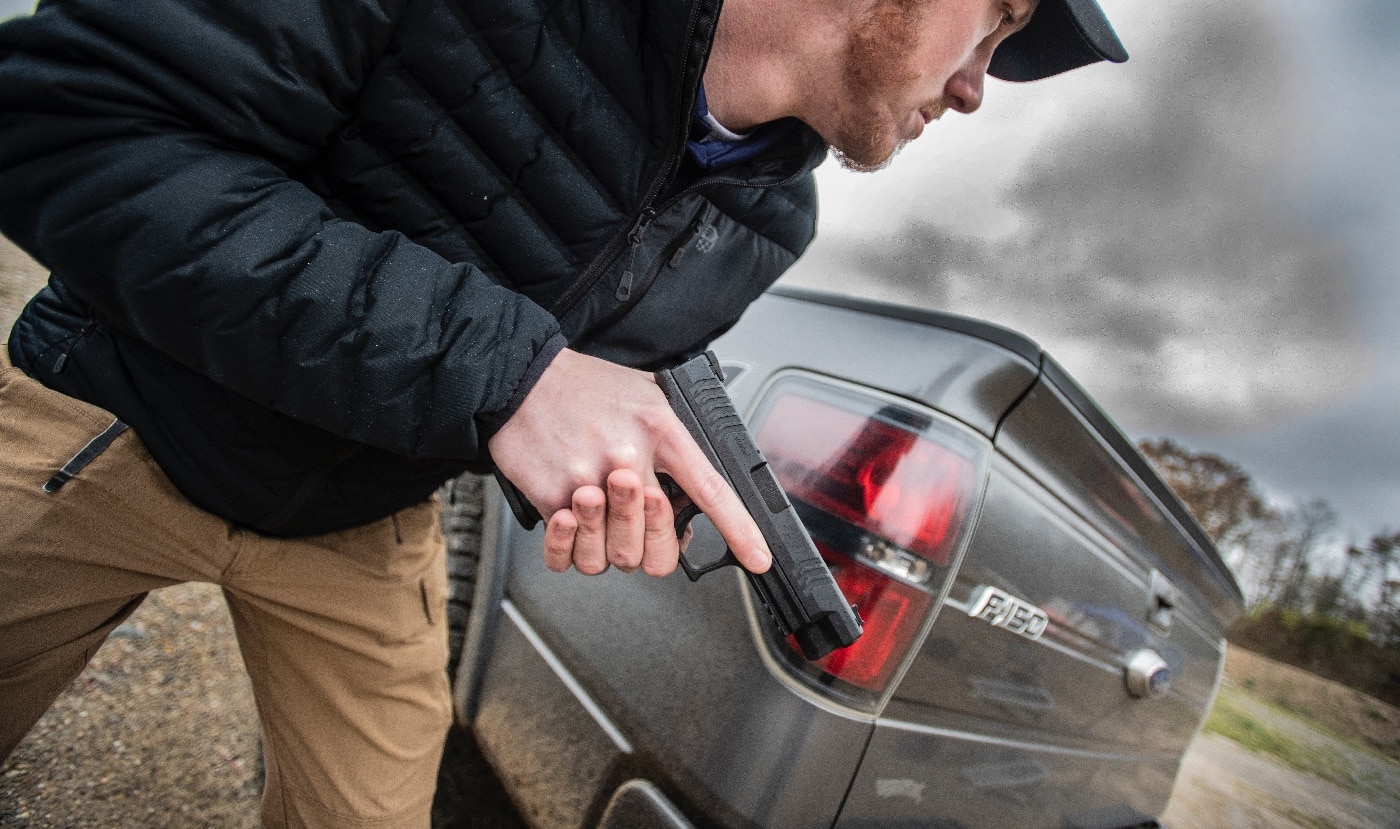 A man, armed with a Springfield Armory XDM pistol, struggles with a carjacker in an intense, close-quarters encounter. The carjacker, dressed in dark clothing, appears aggressive, attempting to overpower the defender near the open driver's side door. The man maintains control of his firearm, demonstrating focus and determination in the life-threatening confrontation. The scene is set in an urban environment, with the truck and surrounding vehicles adding context to the chaotic situation. The tension is palpable, showcasing the critical role of training and situational awareness in self-defense scenarios. The Springfield Armory XDM is clearly visible, emphasizing its reliability as a defensive tool. This image highlights the unpredictability of such encounters and the need for preparedness.