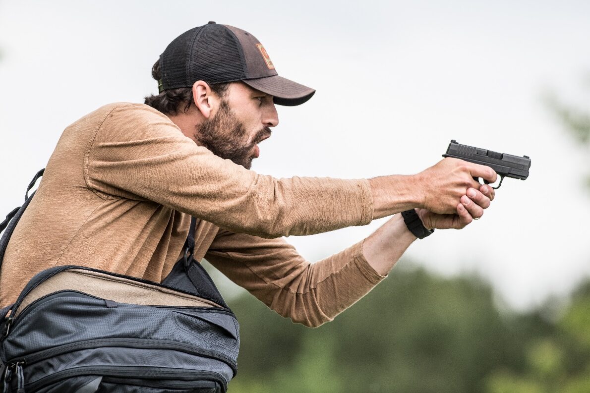 A man stands in his front yard with a determined stance, holding a Springfield Hellcat pistol in both hands as he gives a verbal command to an unseen assailant. His facial expression conveys urgency and fear as he exercises his right of self-defense under Castle Doctrine laws. The setting is a residential property, with a well-maintained lawn and a home visible in the background. The man is asserting his legal right to protect his domicile and loved ones from an immediate threat. Many state laws, including Stand Your Ground statutes, allow homeowners to use force, including deadly force, against unlawful attacks. The legal principle of no duty to retreat applies in some jurisdictions, giving individuals the right to respond with defensive force when faced with imminent danger. In self-defense cases, juries often consider whether the homeowner had a reasonable belief that his life was at risk. The burden of proving justification typically falls on the defense, requiring evidence that lethal force was necessary.