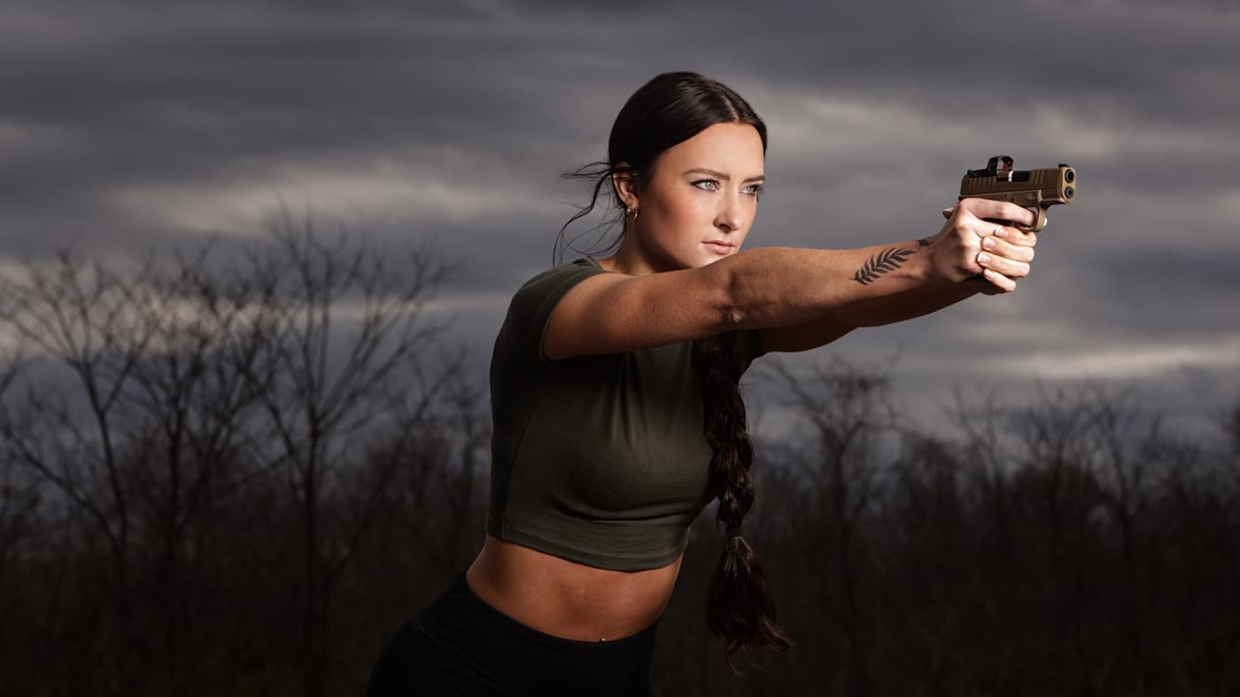 woman with tattoo shooting a semi-automatic pistol at dusk