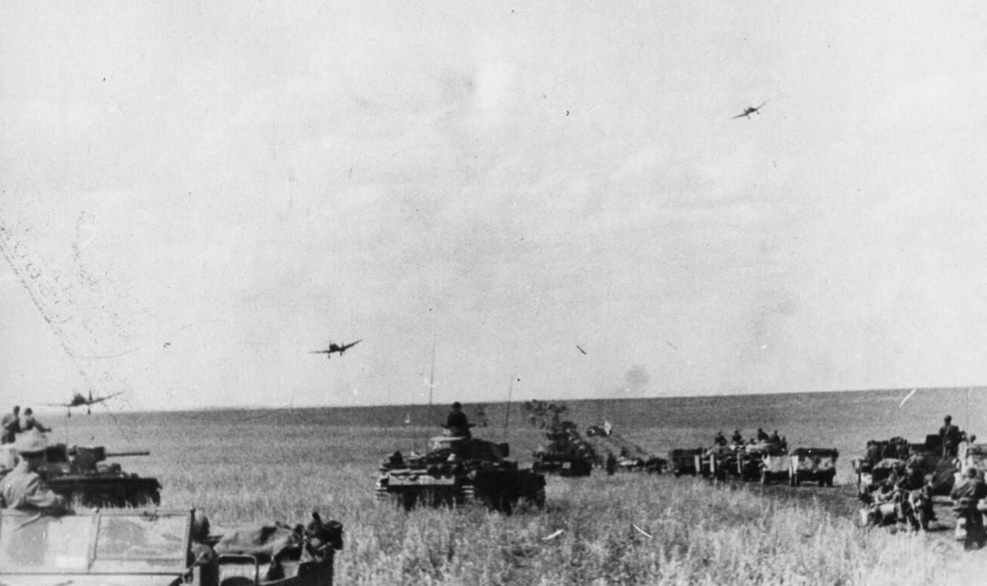 This image captures Junkers Ju 87 Stuka dive bombers returning to base, flying low over an advancing column of German Panzer III tanks and softskin vehicles on the Orel front in July 1943. The dive bombers, with their distinctive inverted gull wings, add a dynamic aerial element to the scene. In the foreground, the Panzer III tanks, also known as Panzerkampfwagen III or pz iii, display their prominent turrets and main armament as they move in formation. The softskin vehicles, part of the logistical support, underscore the combined arms approach characteristic of blitzkrieg tactics. This historic moment vividly illustrates the integration of air and ground power by German armored forces during World War II.